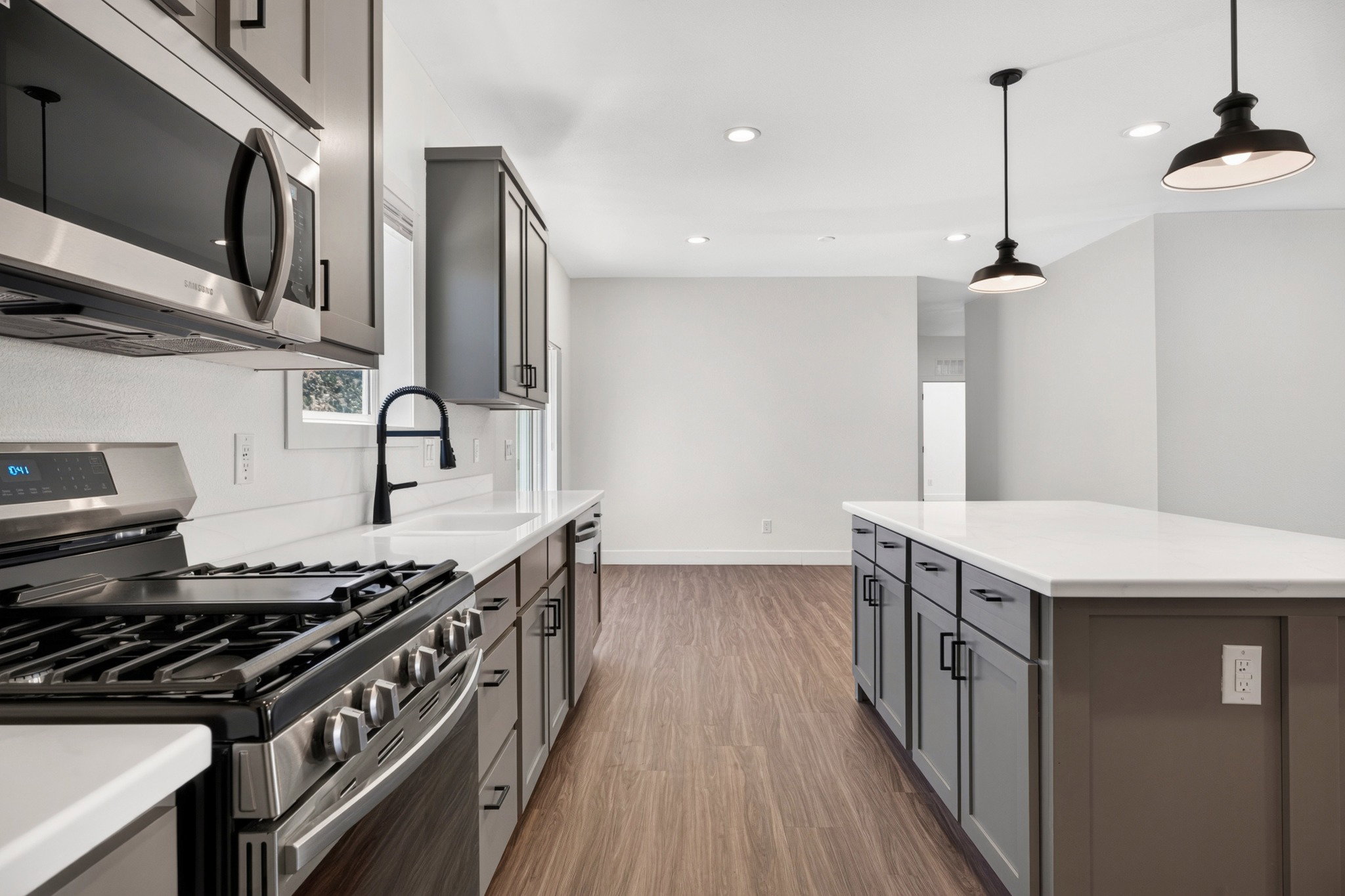 Modern kitchen featuring a gas range, stainless steel appliances, white countertops, dark cabinetry, and wood-finish flooring