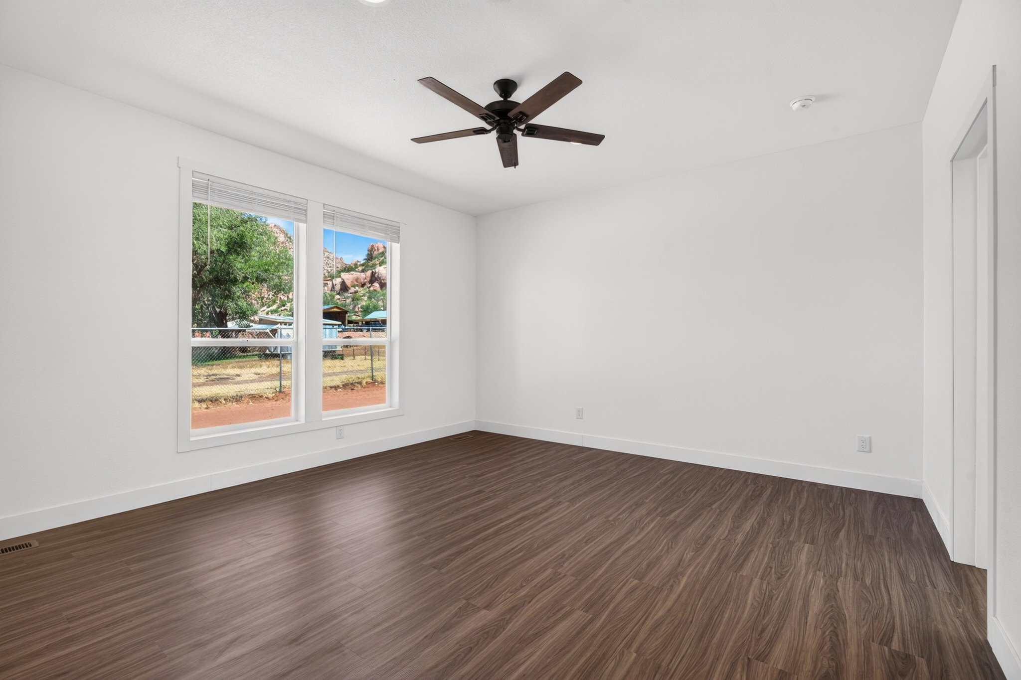 Spacious room featuring wood-finish flooring, white walls, and a dark-toned ceiling fan