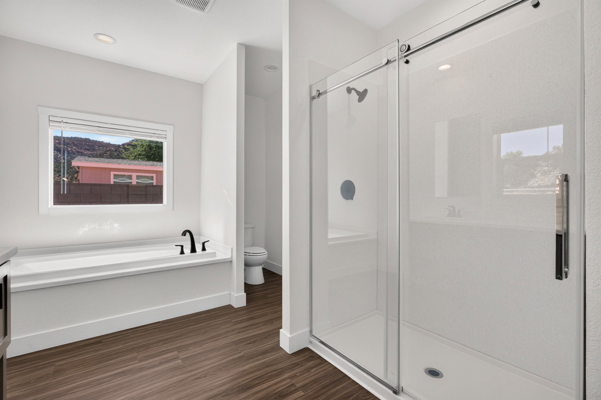 Modern bathroom featuring a glass-enclosed shower, a built-in bathtub with black fixtures, and wood-finish flooring