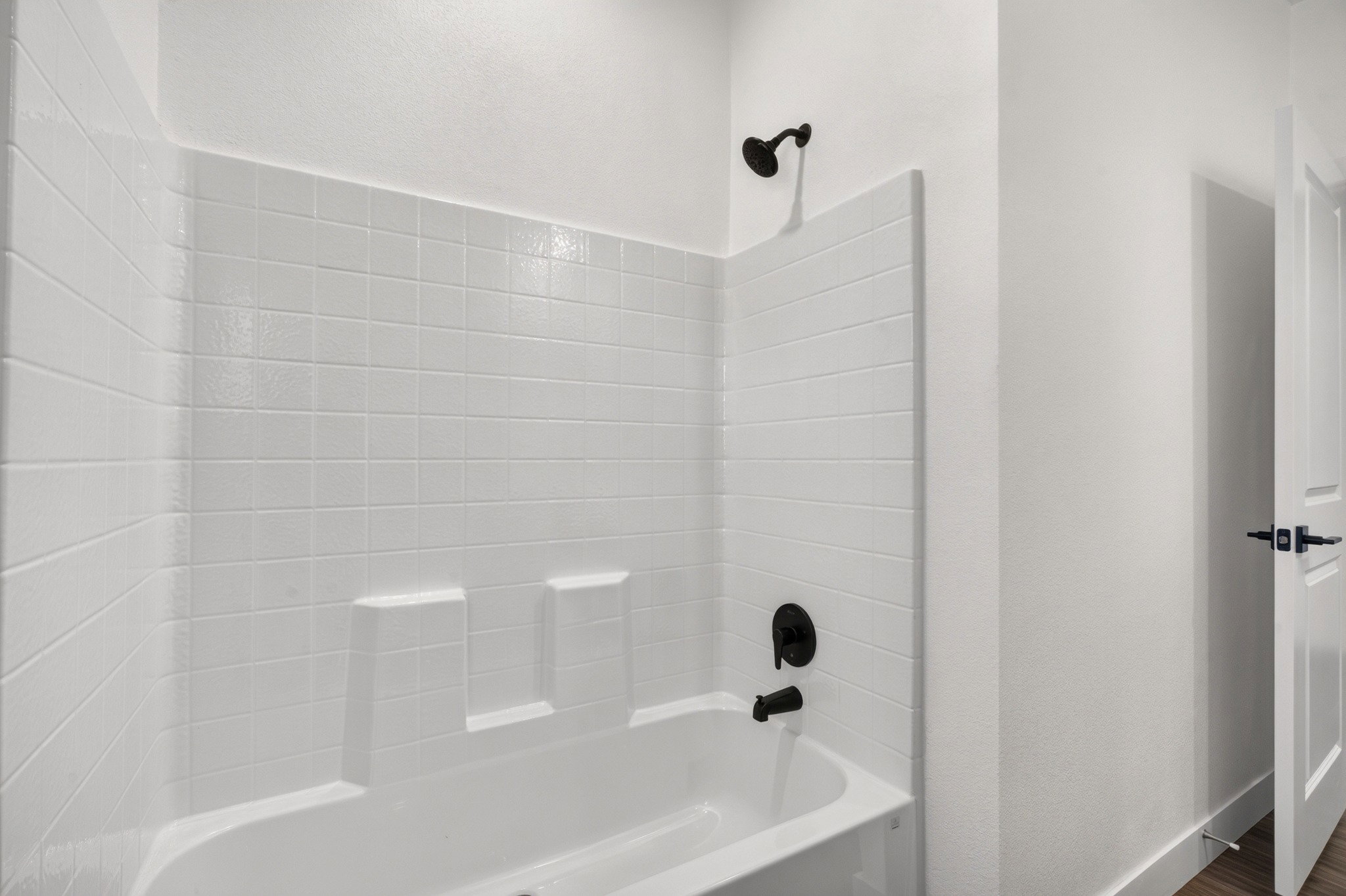 Bathtub and shower combination featuring white subway tile surround, matte black fixtures, and integrated shelving