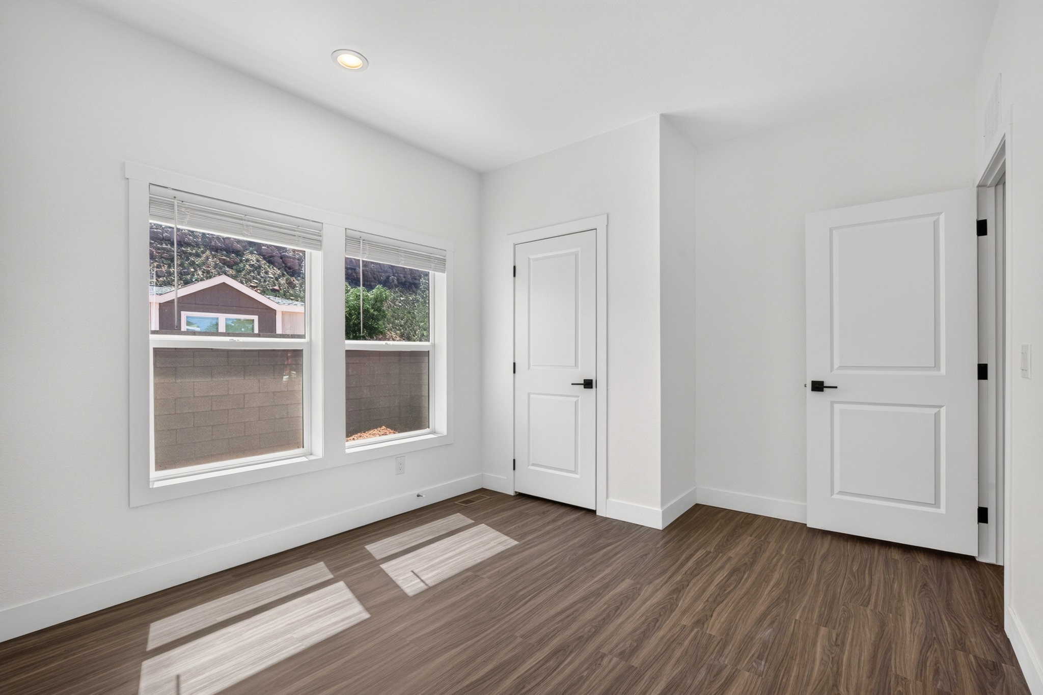 Bright room featuring two windows, wood-finish flooring, recessed lighting, and two panel doors with matte black hardware