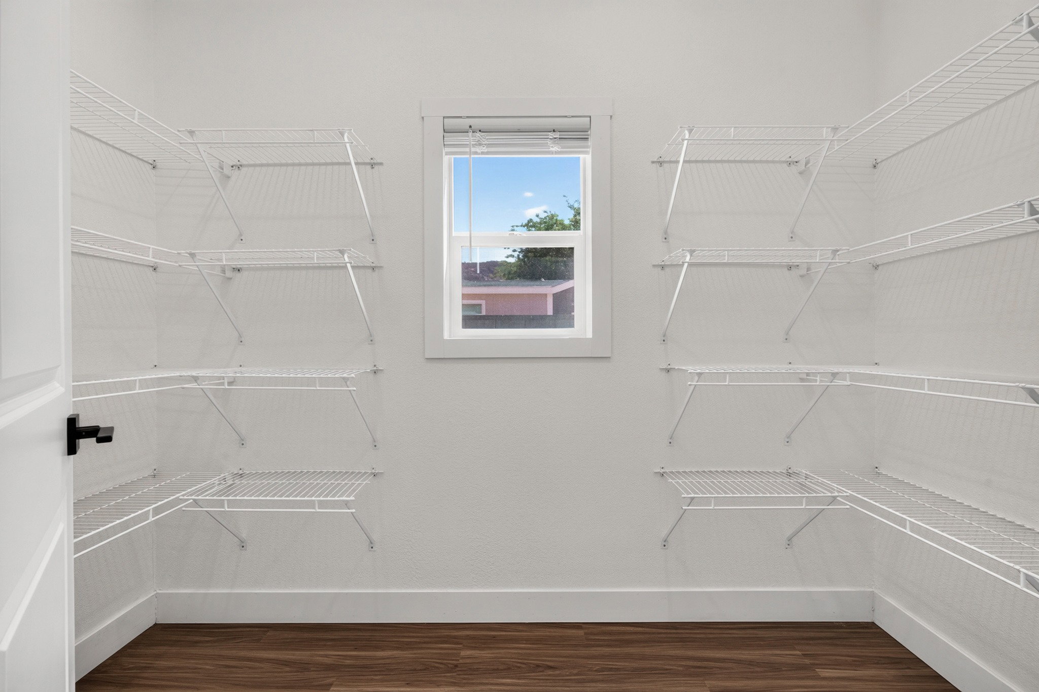 Walk-in closet with extensive wire shelving, wood-finish flooring, and a single window with white trim