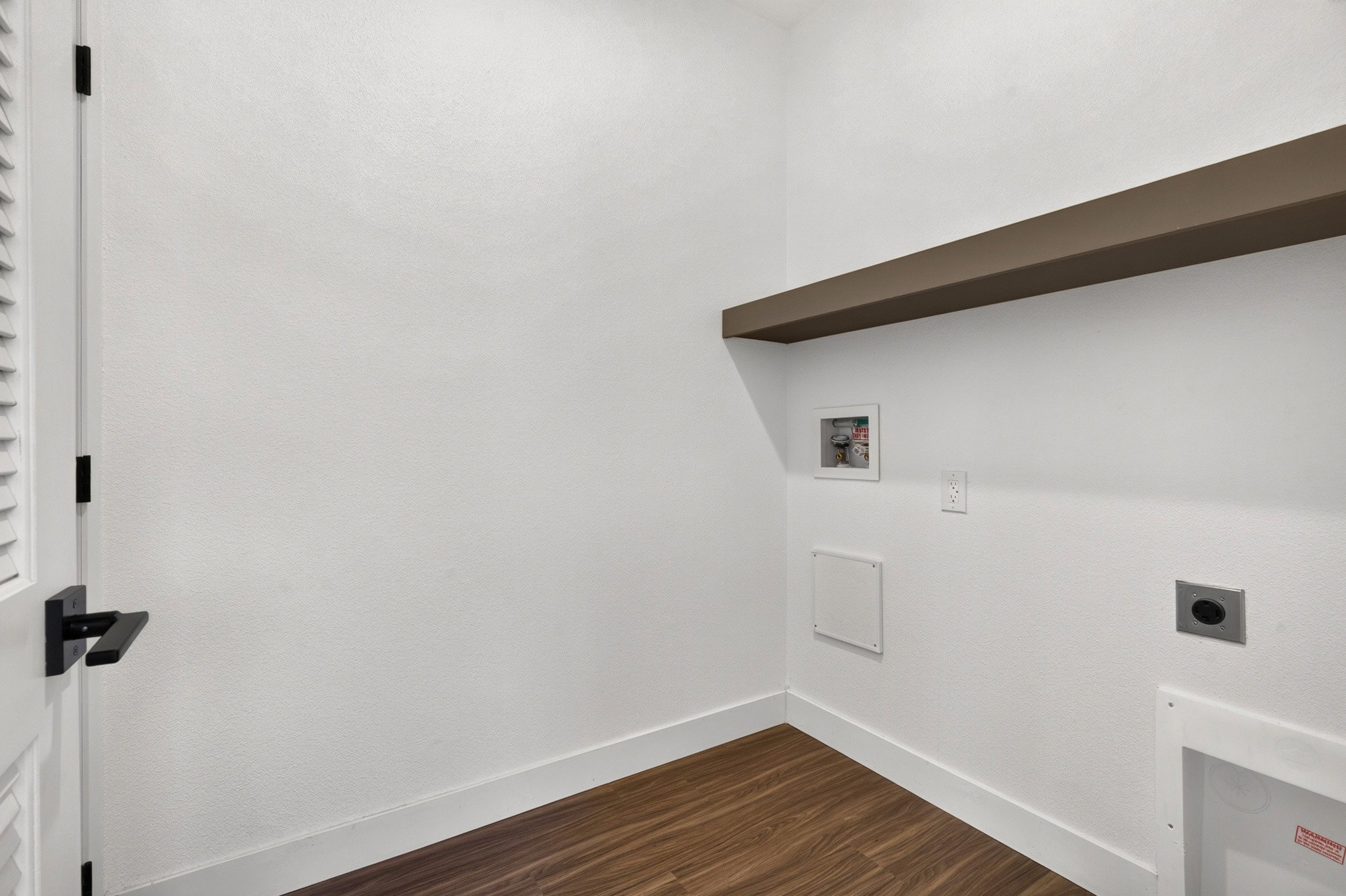 Dedicated utility area with wood-finish flooring, a floating shelf, and white walls