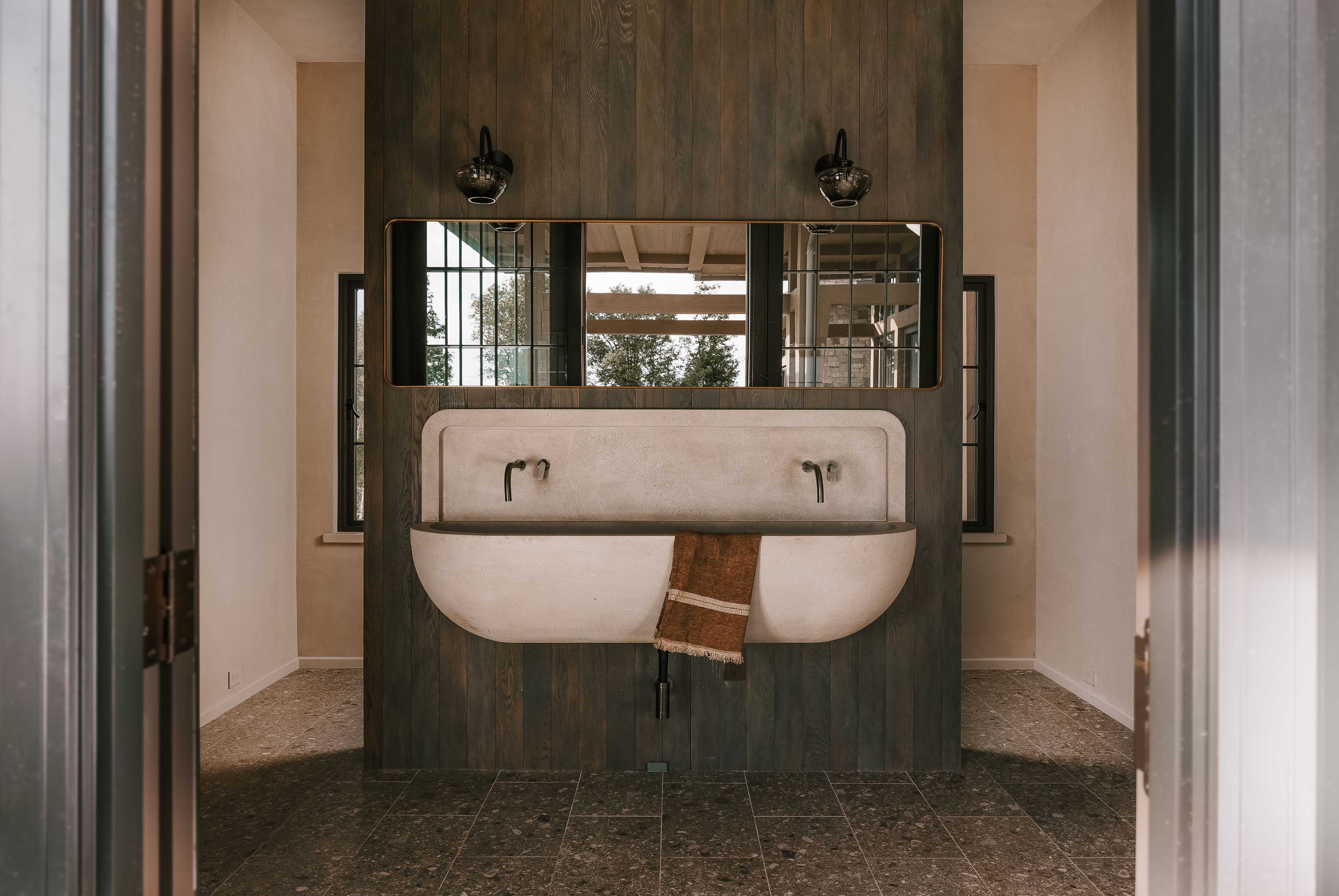 Integrated concrete trough sink with two wall-mounted faucets, set against a dark wood-paneled wall
