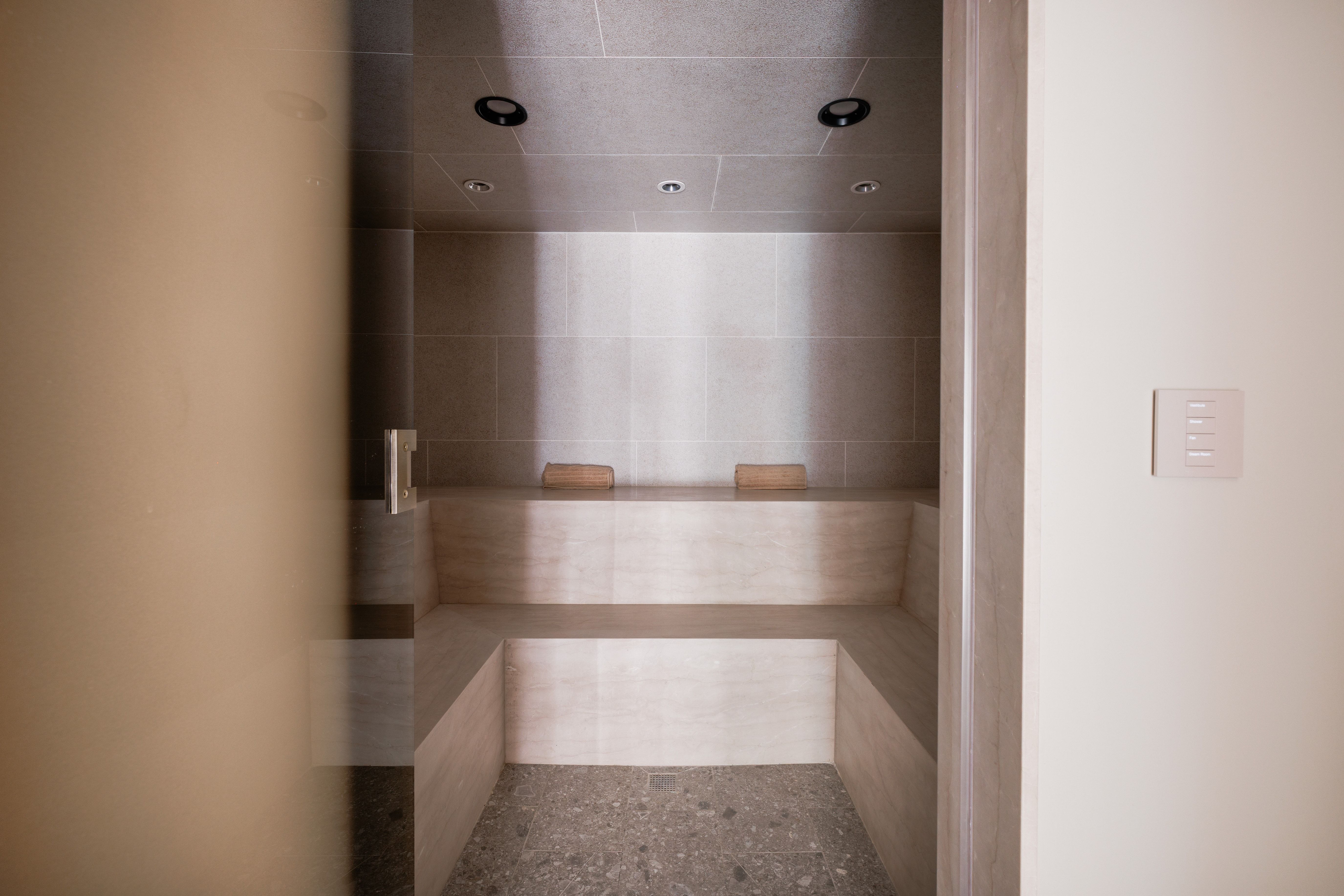 Steam room featuring tiled walls, built-in benches, recessed lighting, and a pebble-finish floor