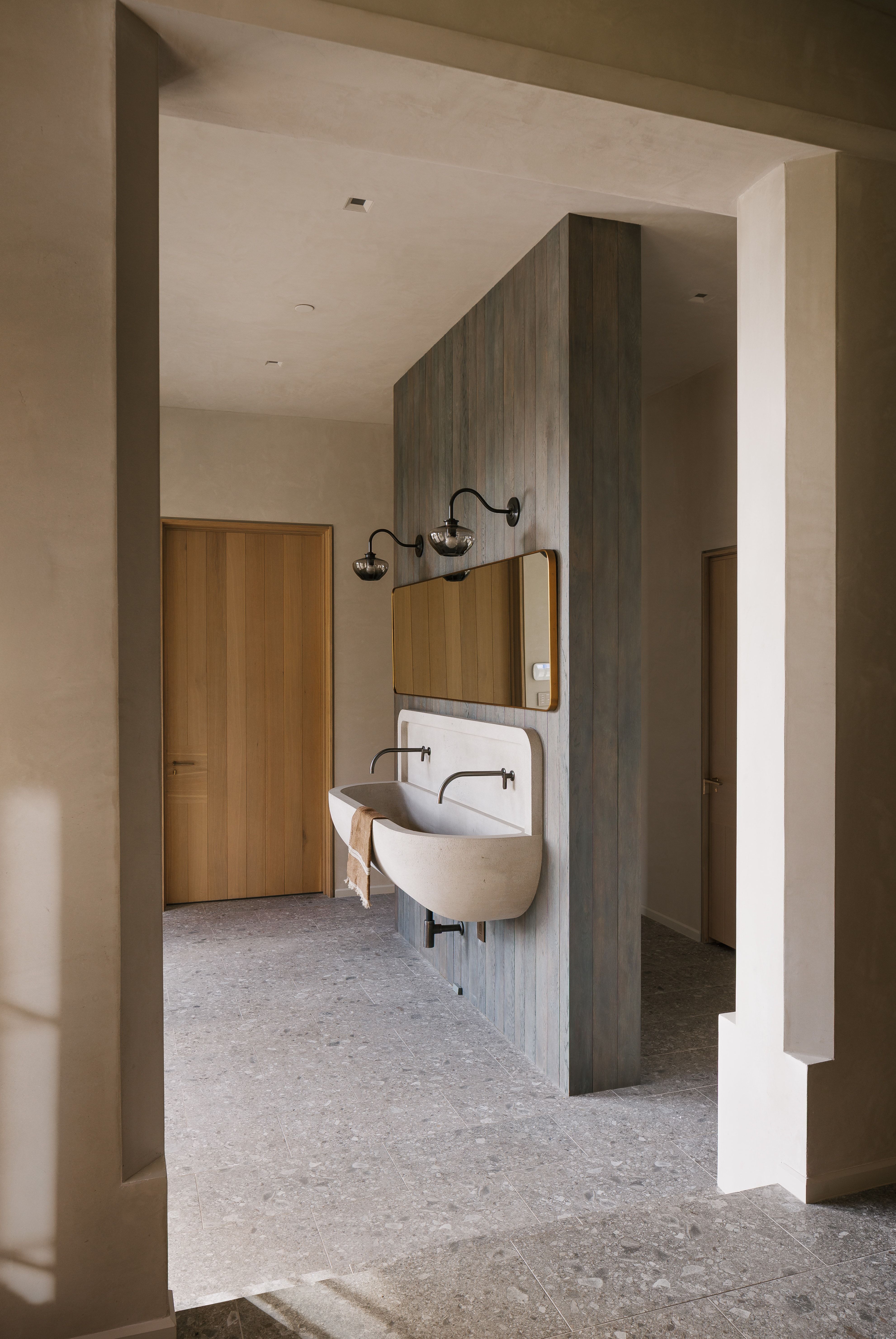 Stone double basin vanity with matte black wall-mounted faucets, accented by a wood-paneled partition