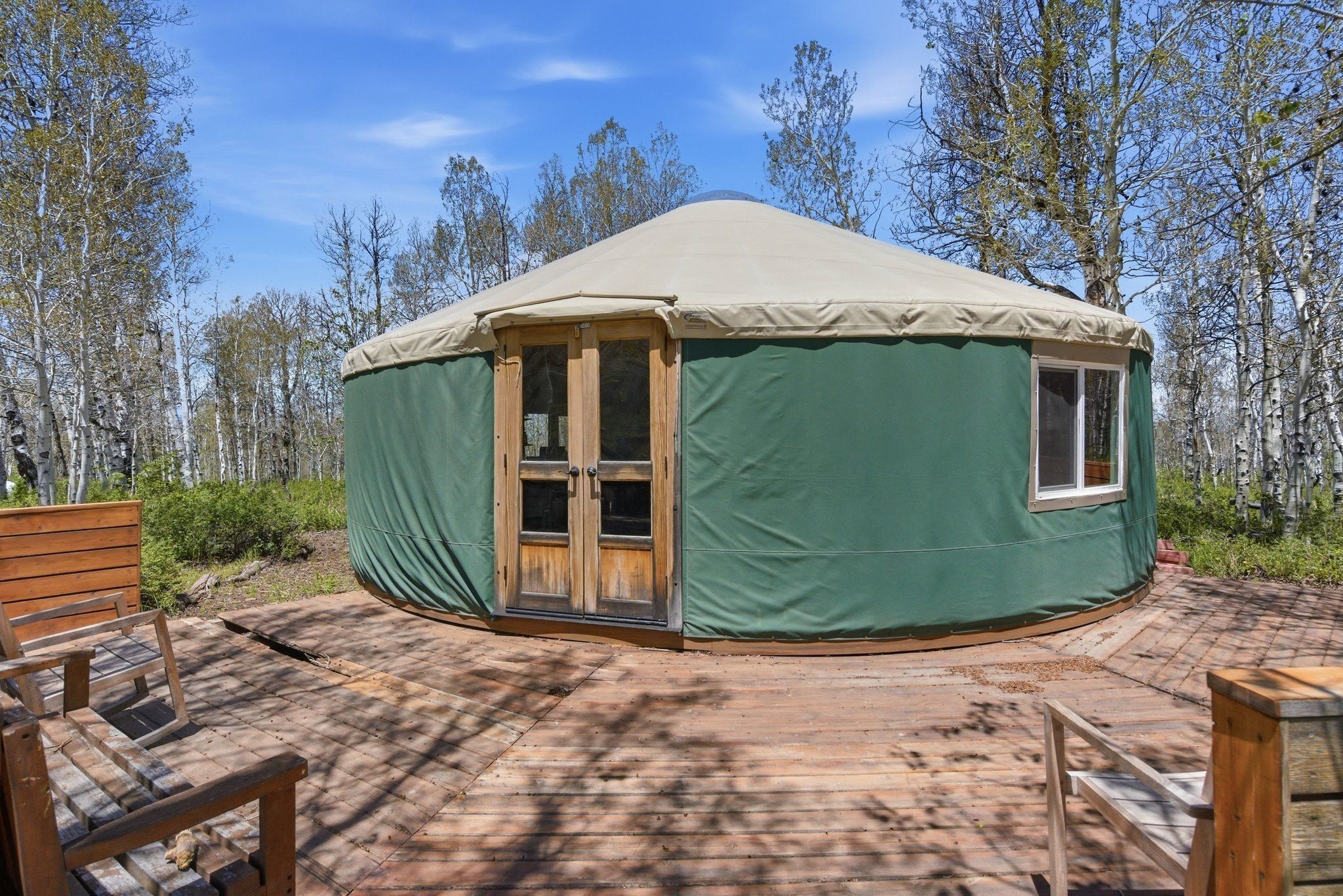 Green yurt structure with a light-colored roof and a wooden base