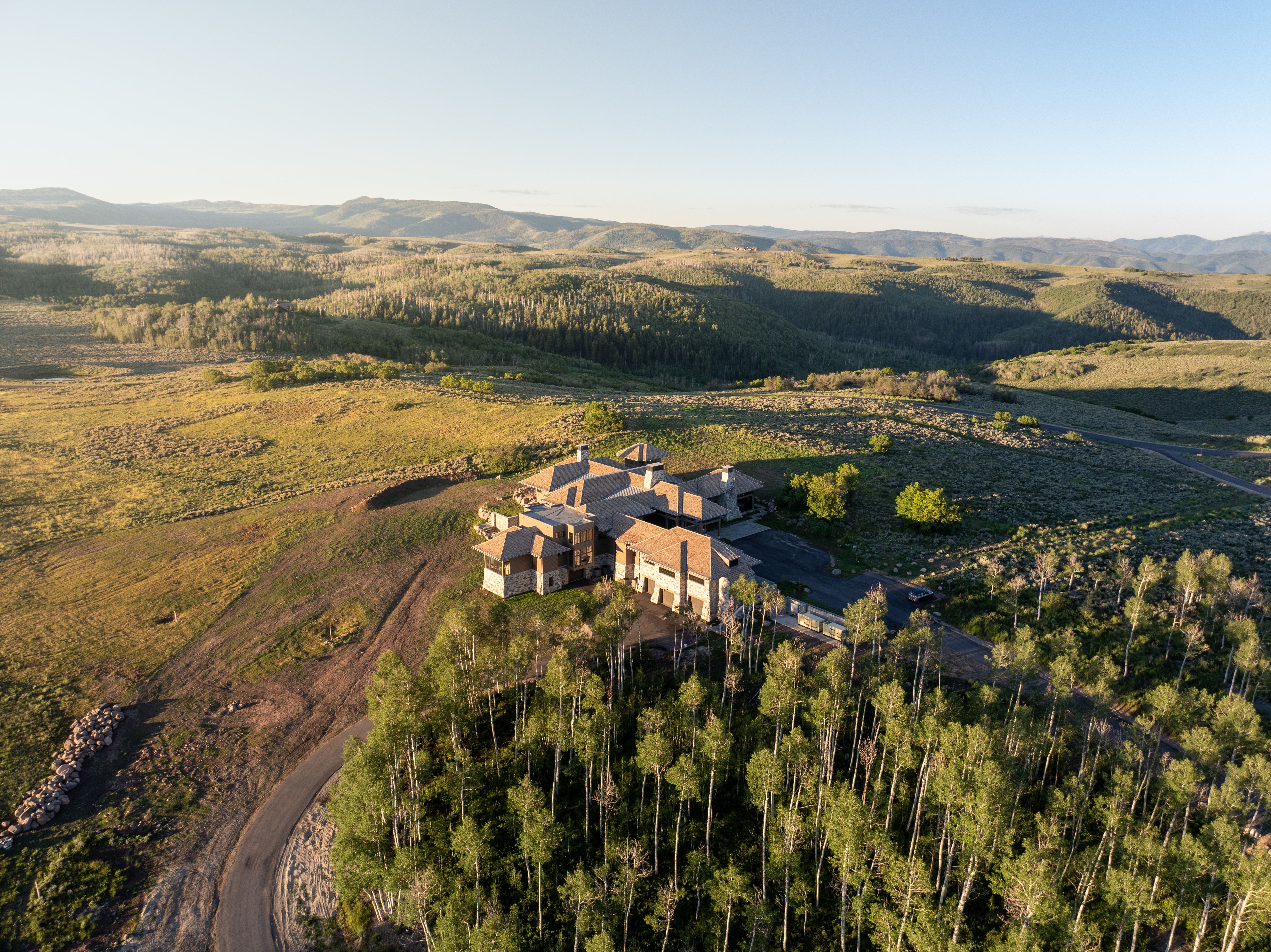 Expansive property featuring a multi-level residence with stone and stucco exterior, multiple chimneys, and a dark roof
