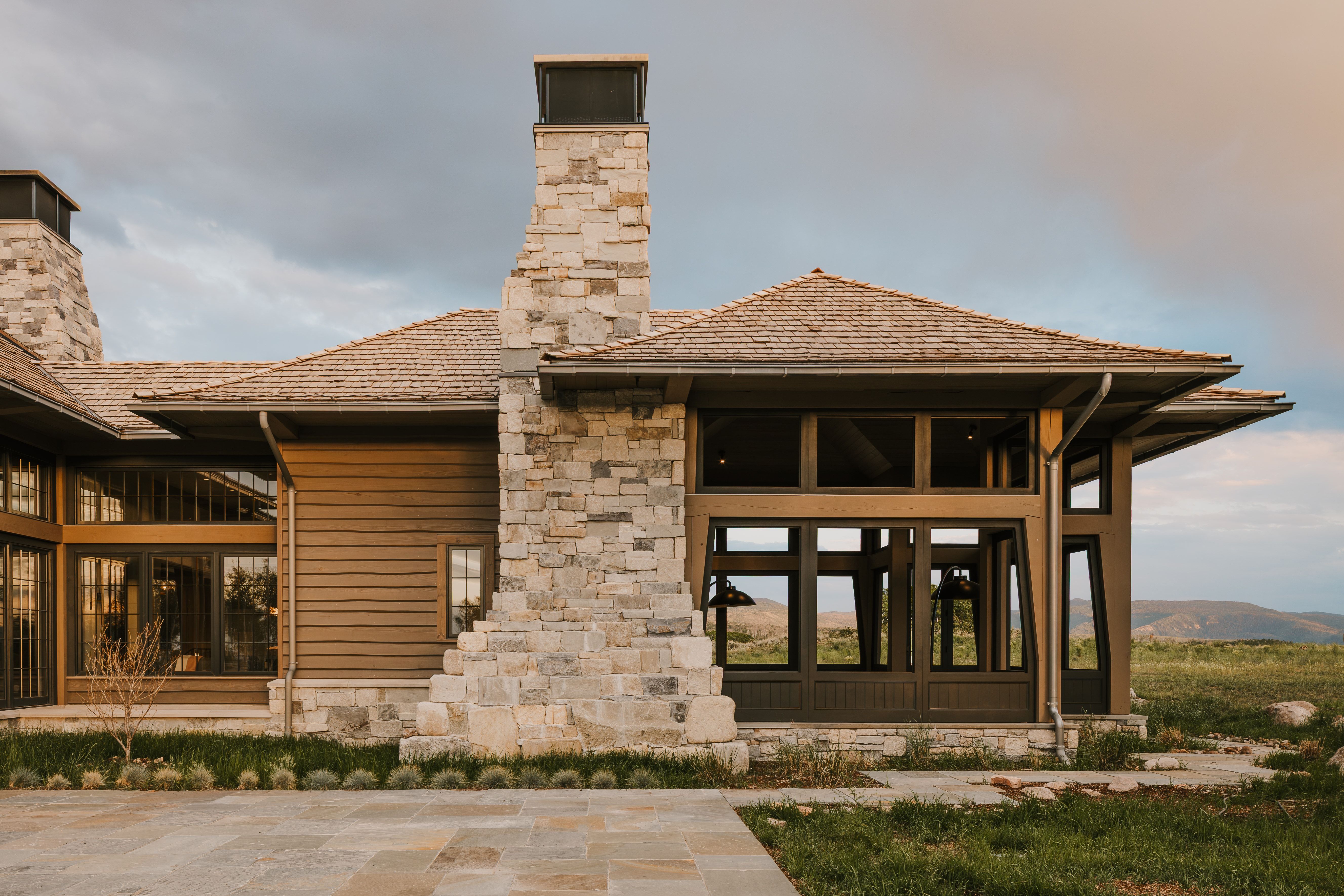 Contemporary architecture featuring a wood shake roof, stone chimneys, and expansive window walls
