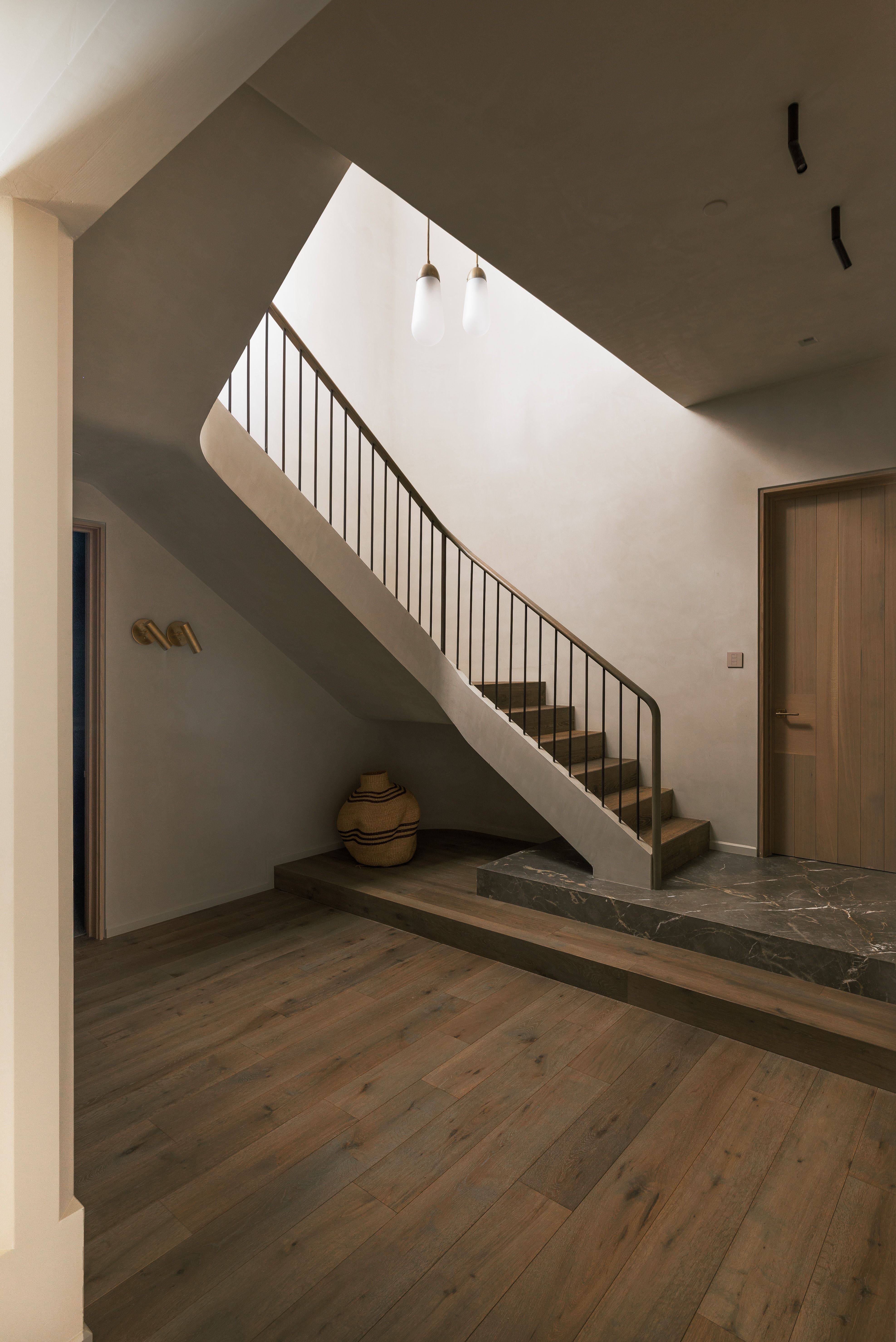 Curved staircase with dark metal railing, wood-finish flooring, and a marble-finish landing