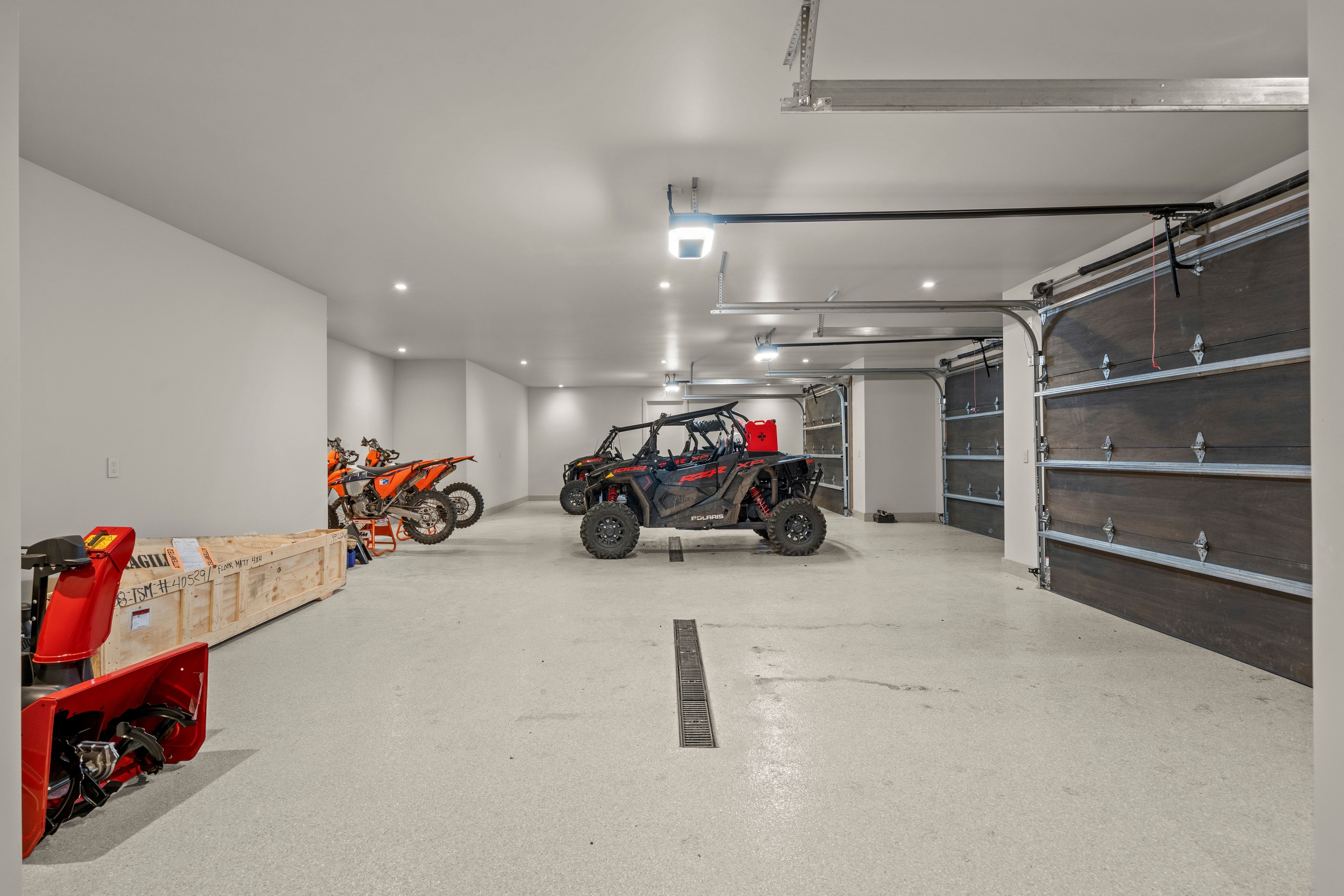 Spacious multi-bay garage featuring a light-colored epoxy floor coating, recessed lighting, and dark wood-finish garage doors