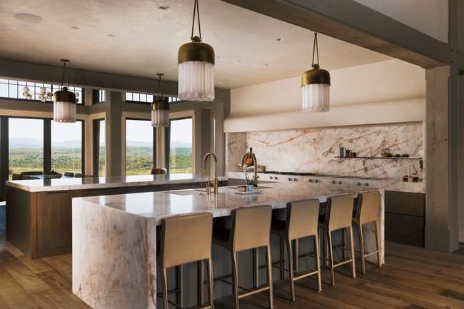 Kitchen featuring a waterfall island, integrated cooktop, full-height stone backsplash, wood-finish flooring, and multiple pendant light fixtures