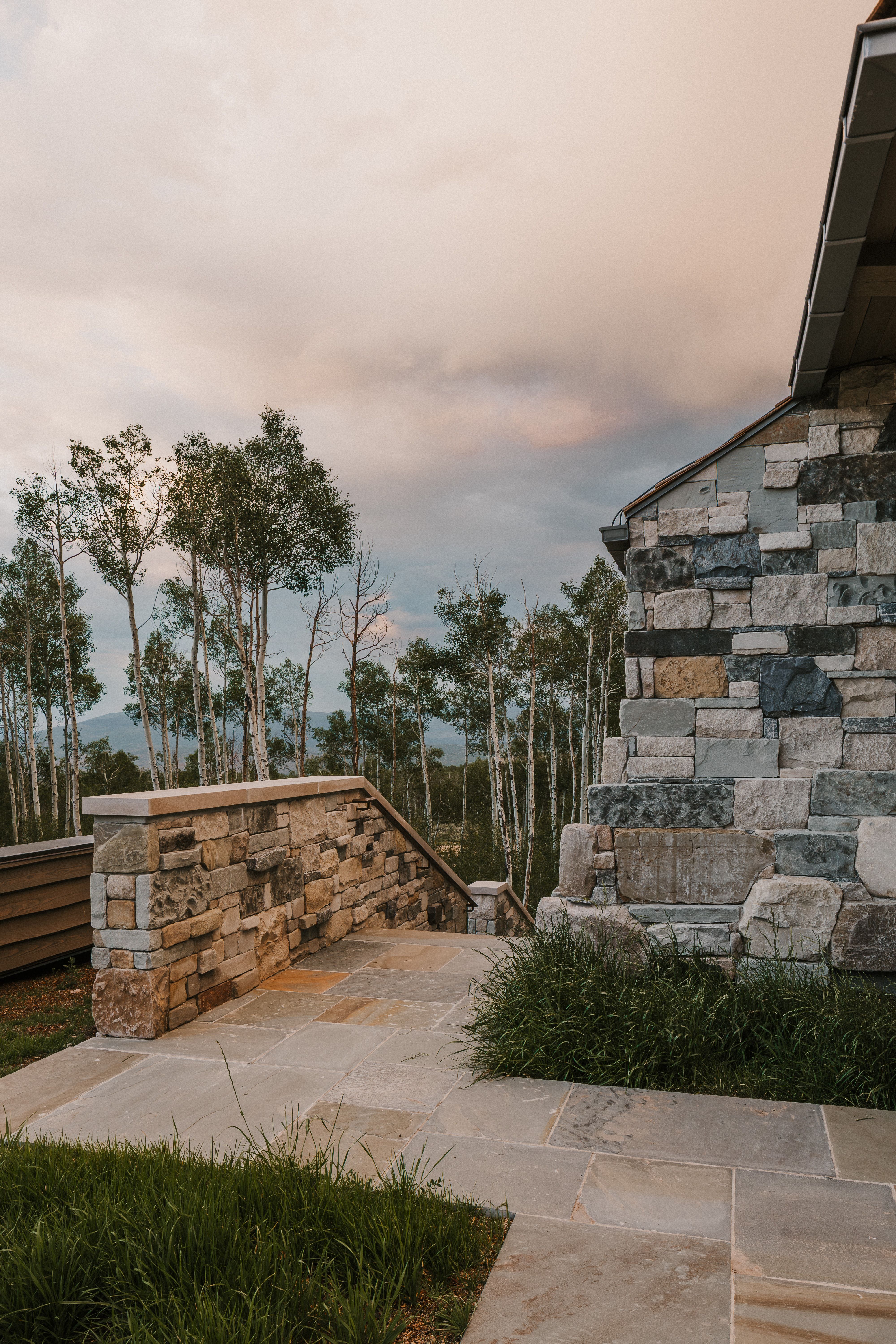 Stone exterior with varied natural hues, featuring a stone retaining wall and a flagstone patio
