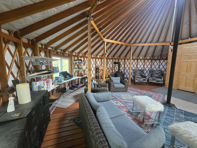 Circular structure featuring exposed wood beams, a central wood-burning stove, and wood-finish flooring
