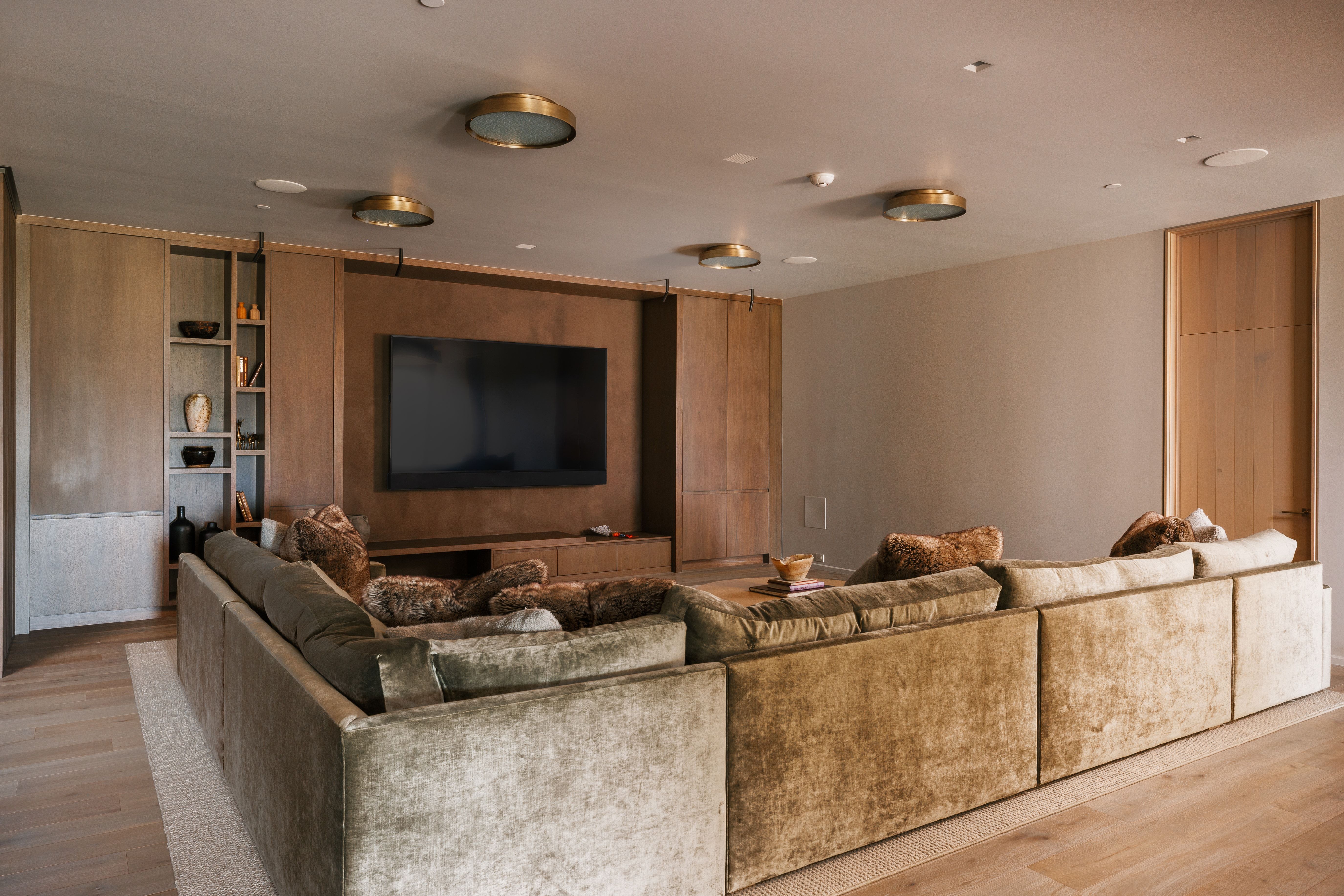 Integrated wall-mounted television with built-in media console, custom cabinetry, recessed ceiling lights, and light wood-finish flooring