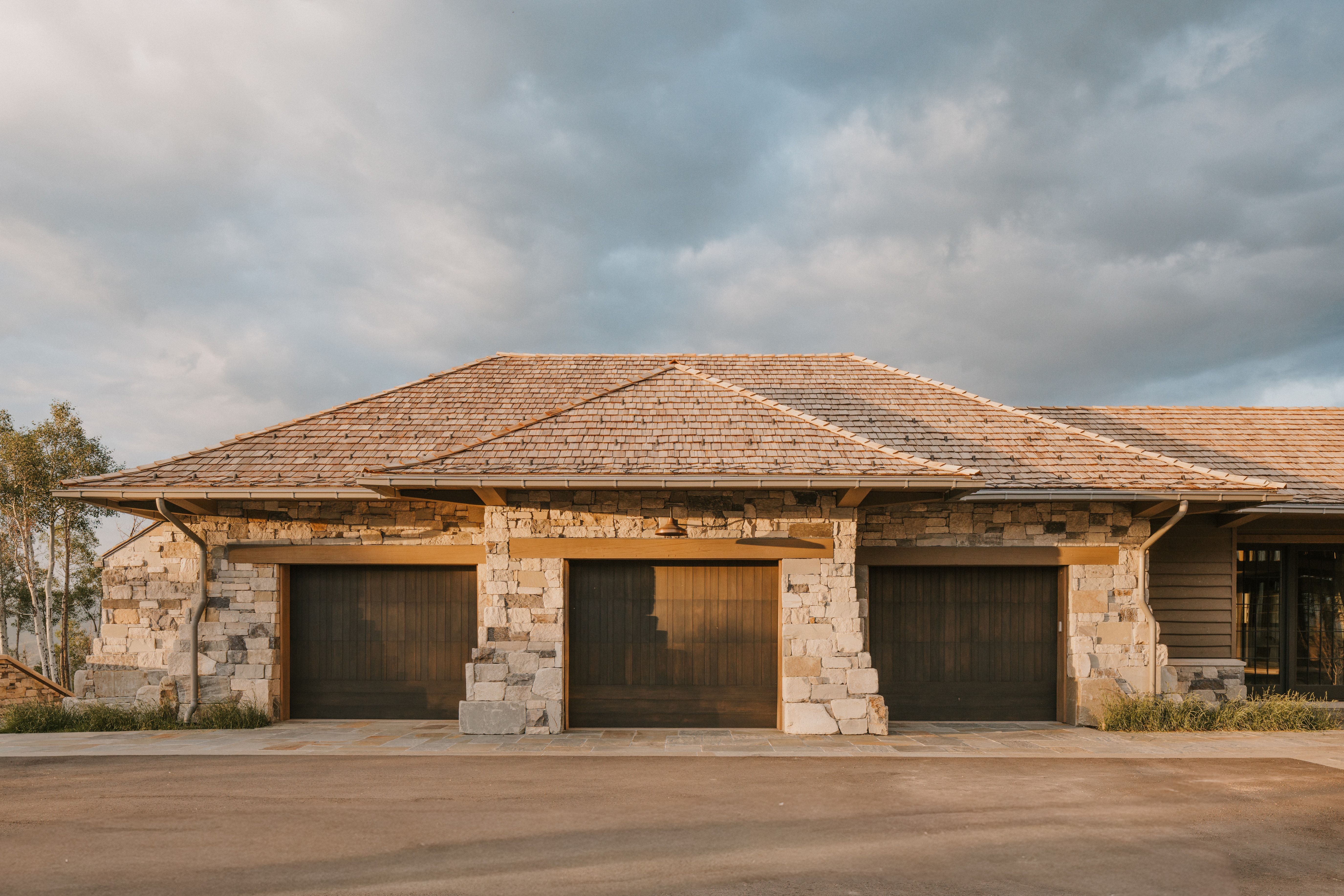 Three-car garage featuring wood-finish doors and stone pillar accents