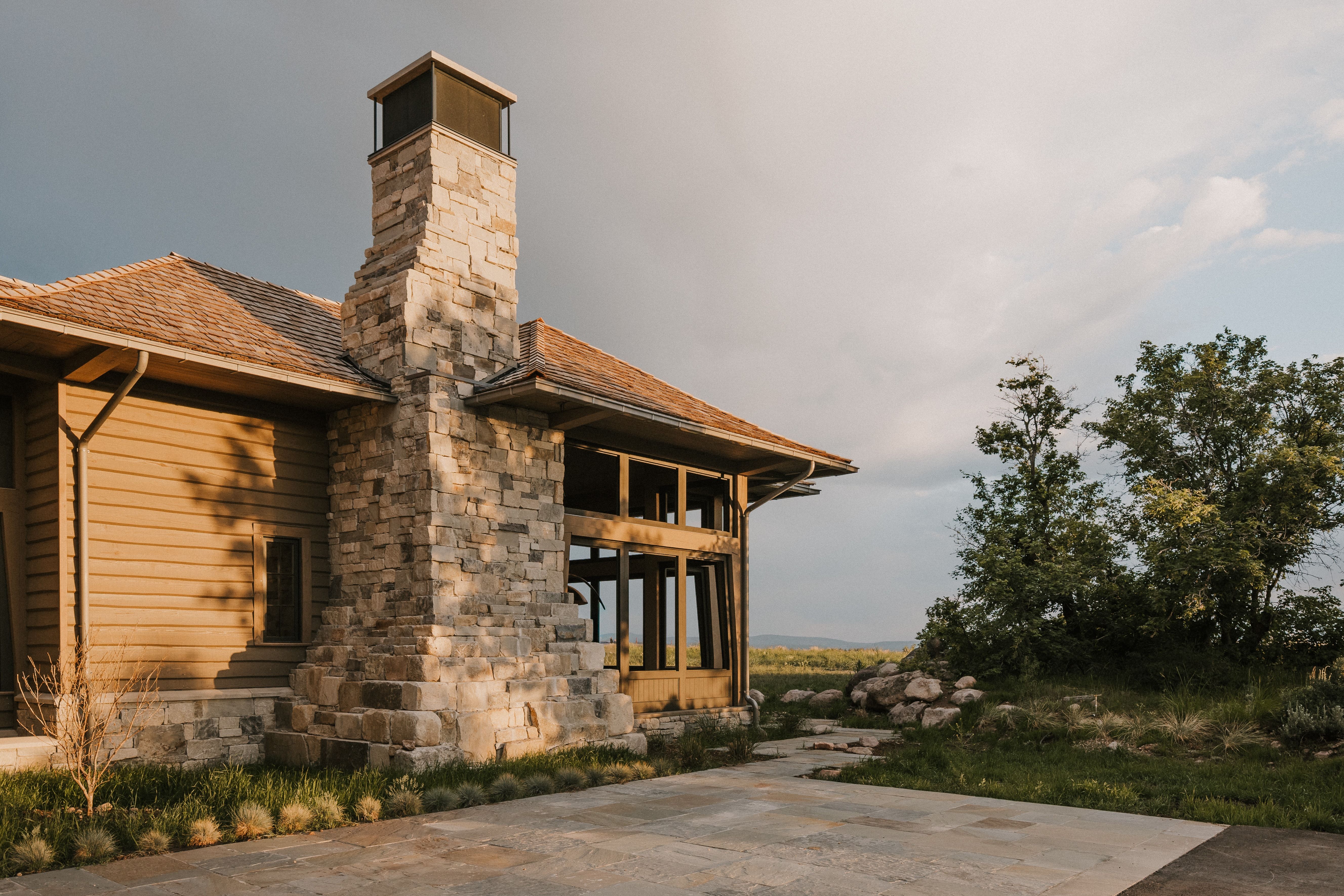 Exterior stone chimney with a metal cap, horizontal siding, and a gabled roof