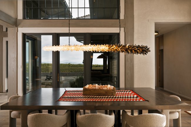 Dining area featuring a linear chandelier with a crystal-like design, expansive glass doors, and a second-story interior balcony with metal railings