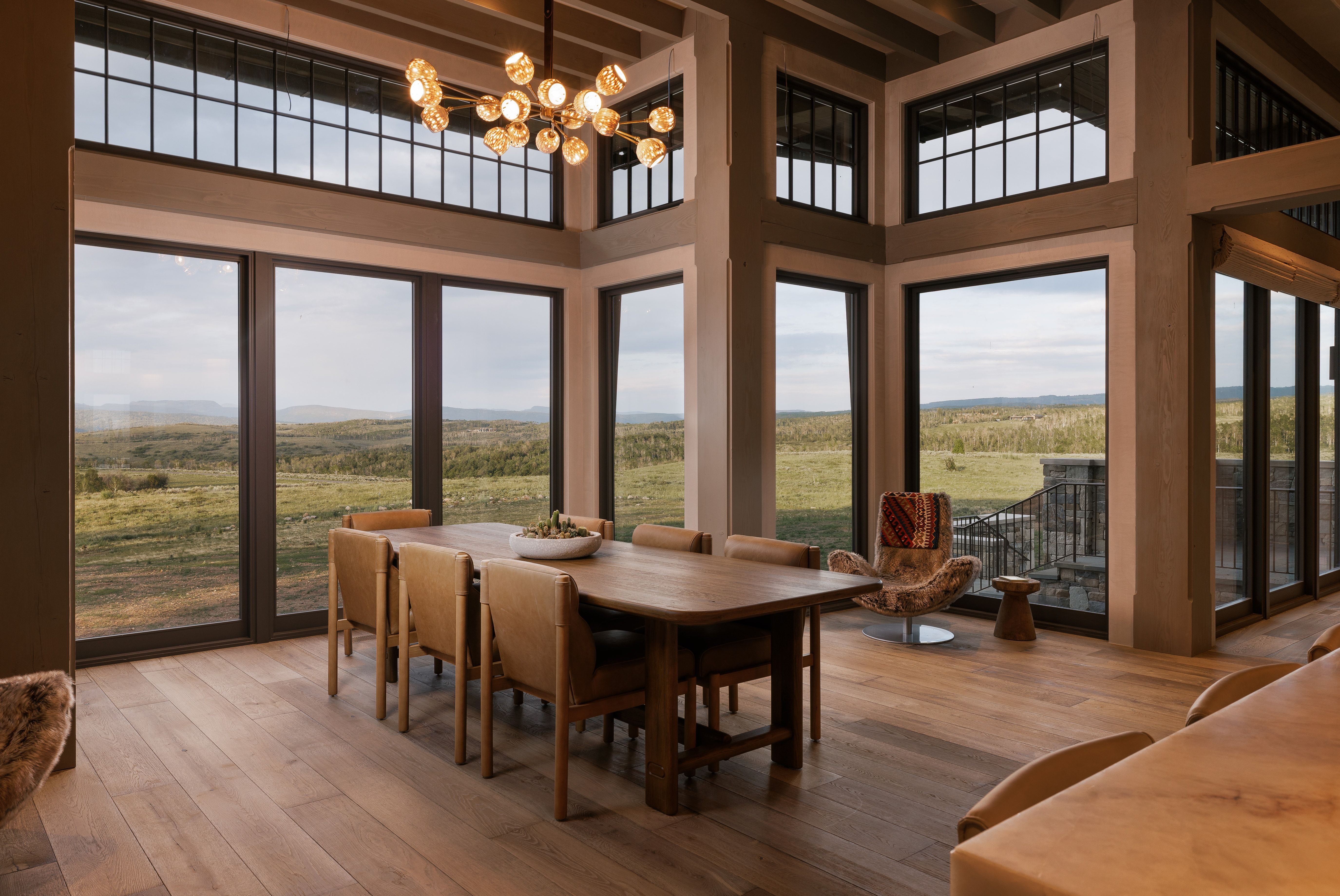 Spacious dining area featuring expansive windows, wood-finish flooring, exposed ceiling beams, a contemporary multi-bulb chandelier, and a substantial wood dining table