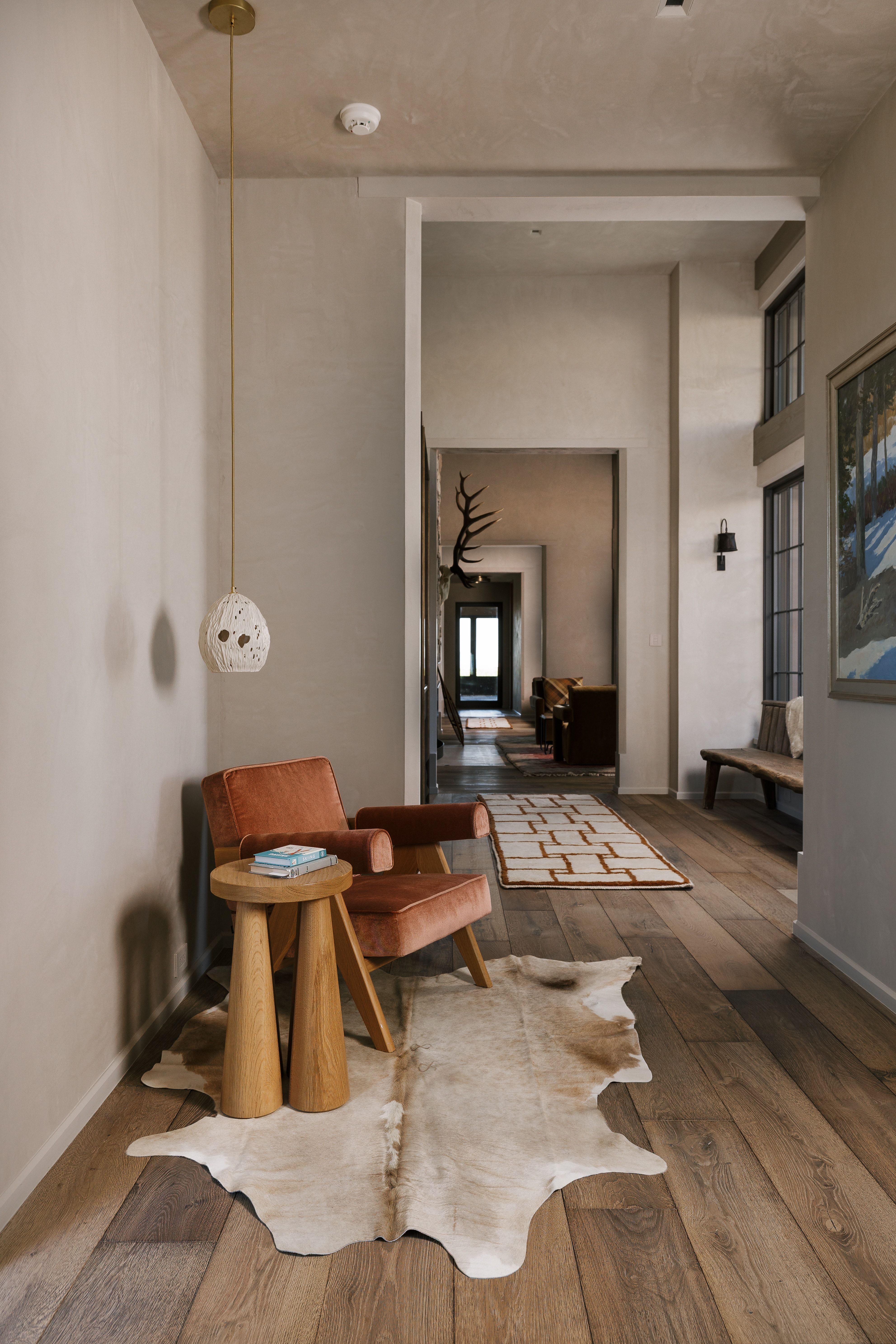 Wide plank wood-finish flooring extending into an open hallway, accented by a distinctive pendant light fixture