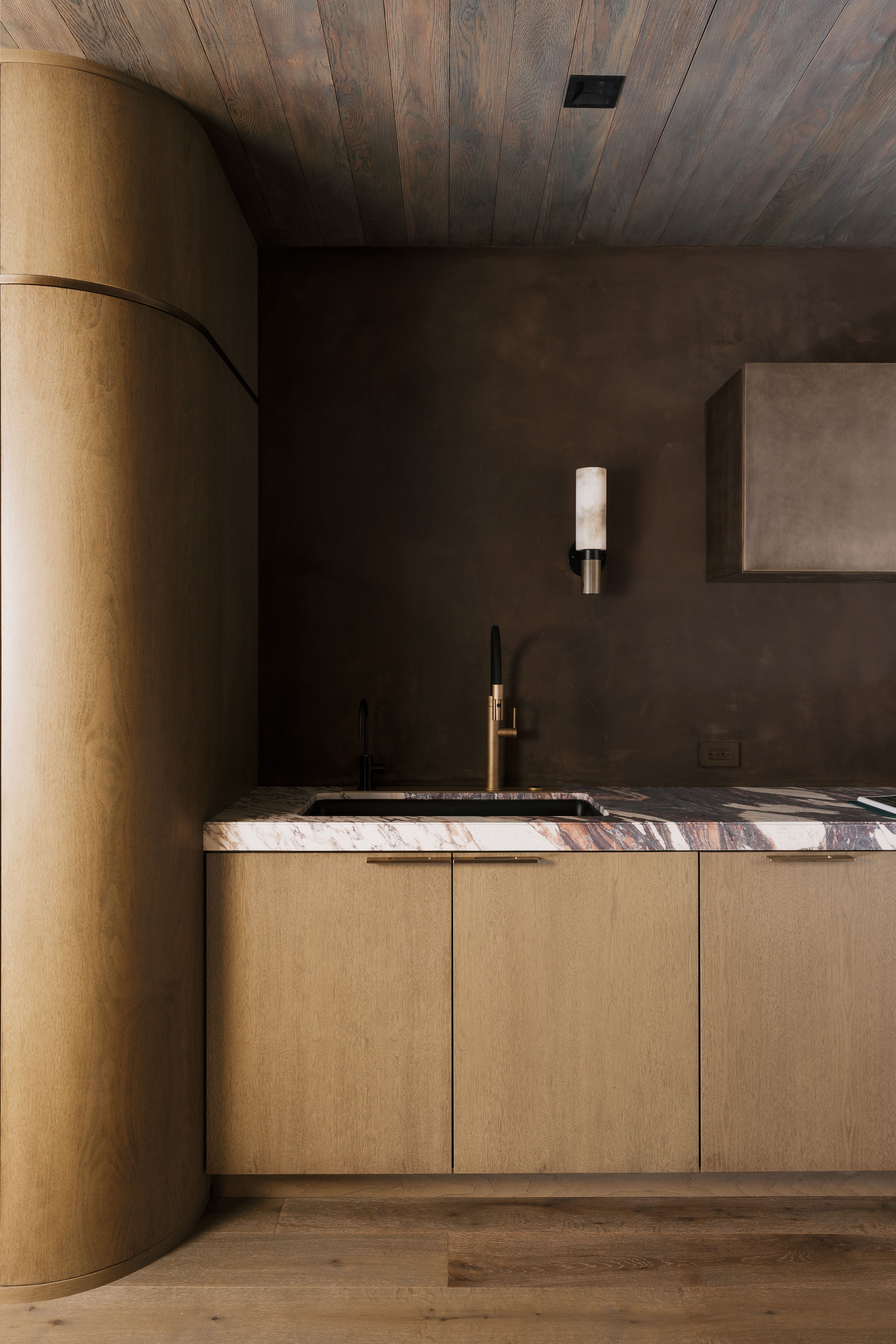 Custom wood-finish cabinetry featuring integrated hardware, a contrasting stone countertop with an under-mount sink, and a modern wall-mounted faucet