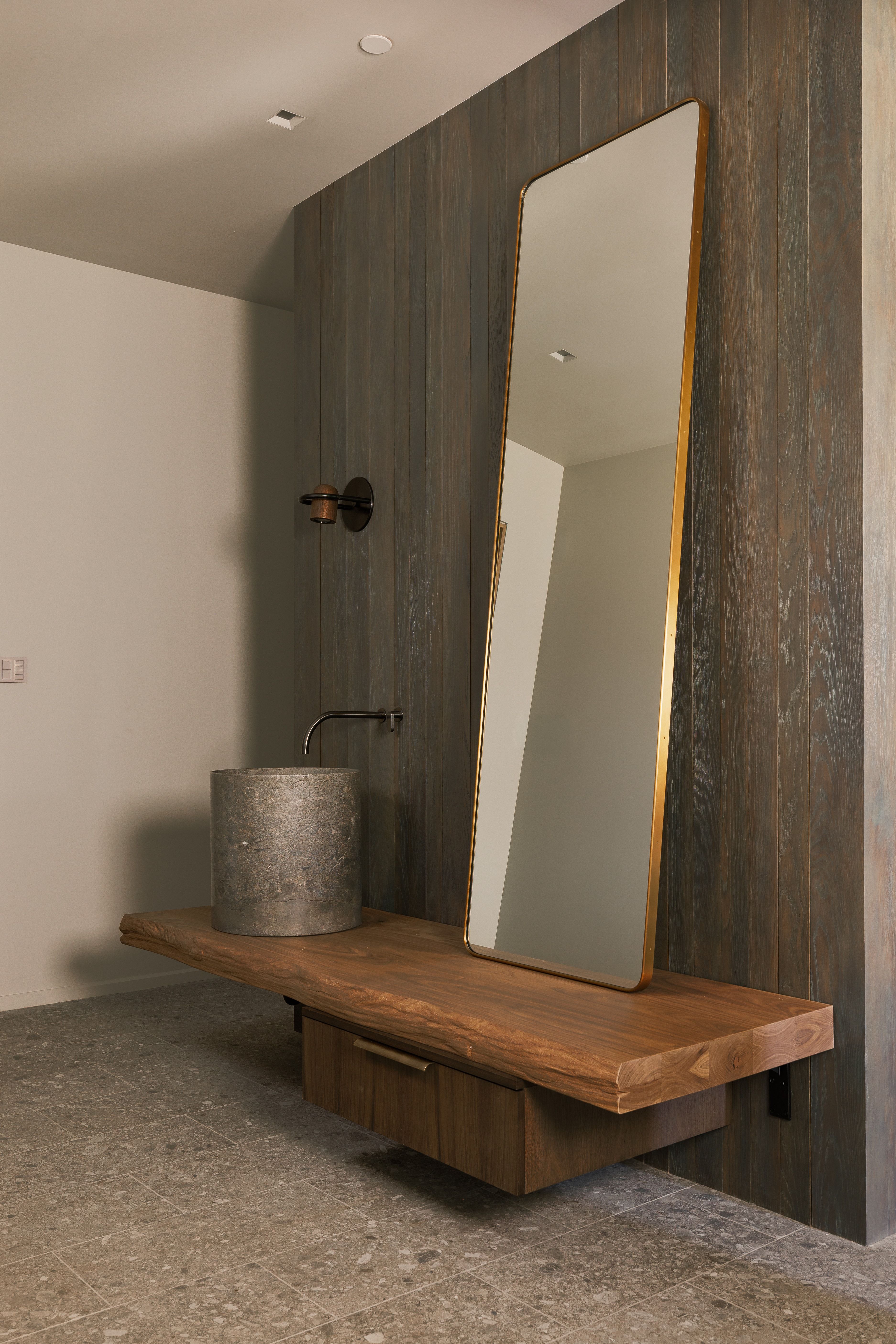 Floating wood-finish vanity with an integrated drawer, complemented by a stone vessel sink and wall-mounted faucet