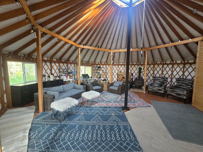 Open-concept living space featuring a central skylight, exposed wood beams, and a wood-burning stove