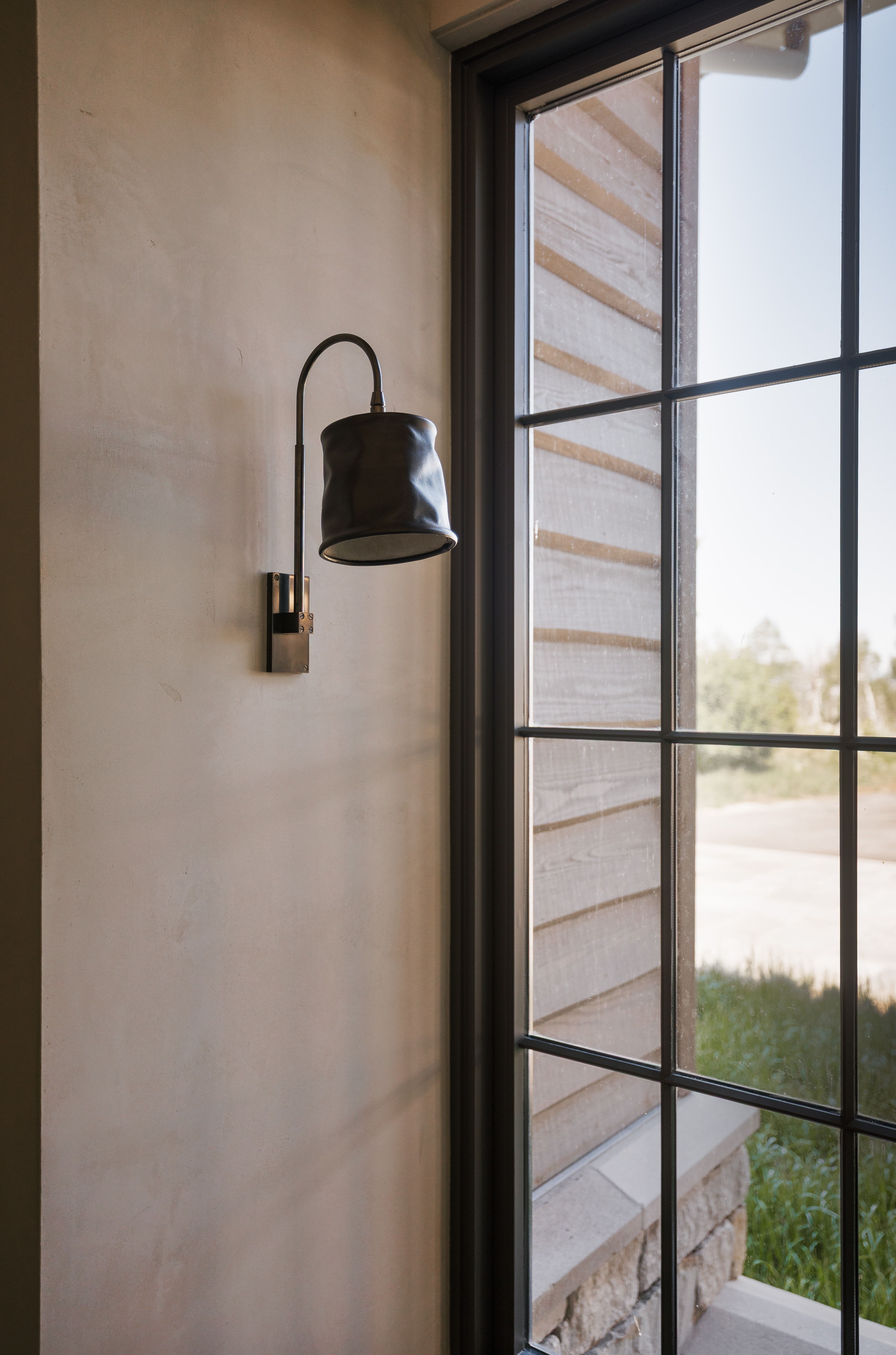 Accent wall sconce with a dark metal finish and unique shade design, featuring smooth plaster wall texture
