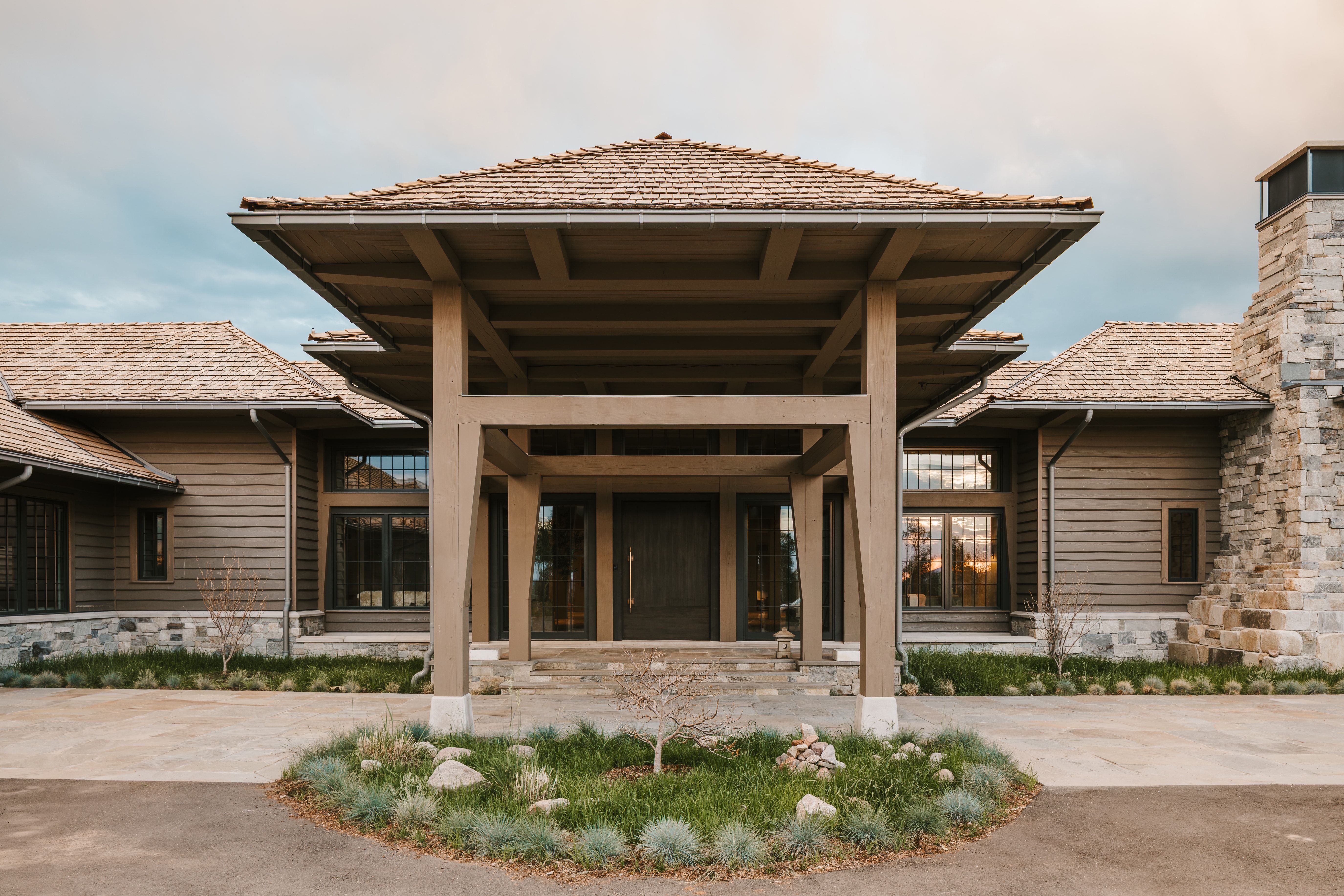 Architectural residence featuring a prominent covered entry, wood shingle roofing, horizontal siding, stone veneer foundation, and a stone chimney