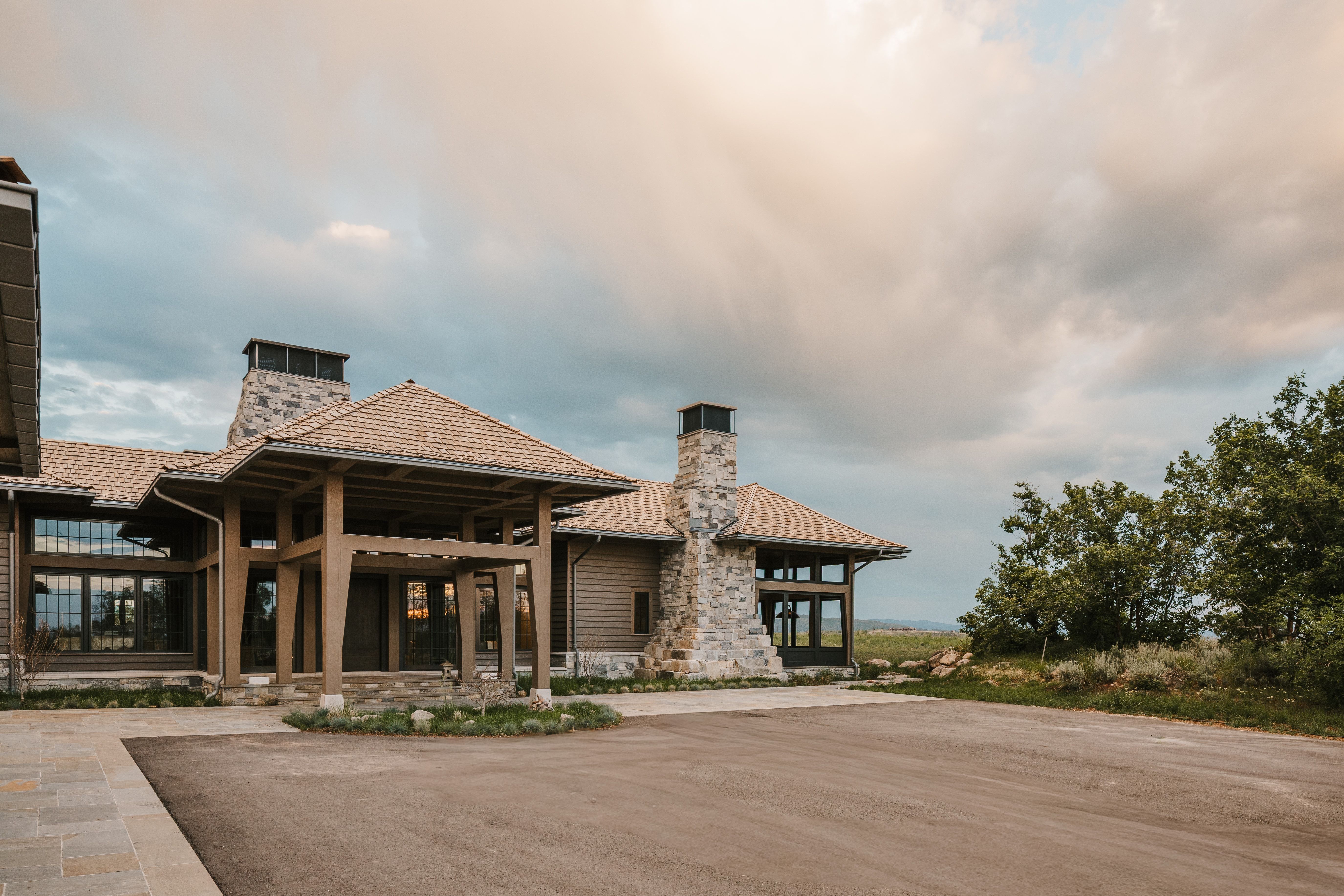 Wood-sided residence featuring a prominent stone chimney and a covered entry with timber columns