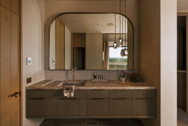 Floating vanity with wood-finish cabinetry, integrated stone sink, and countertop with an arched framed mirror