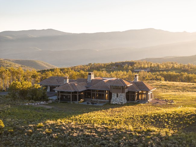 Expansive residence featuring a stone and wood exterior with multiple gabled roofs, prominent chimneys, and extensive glazing