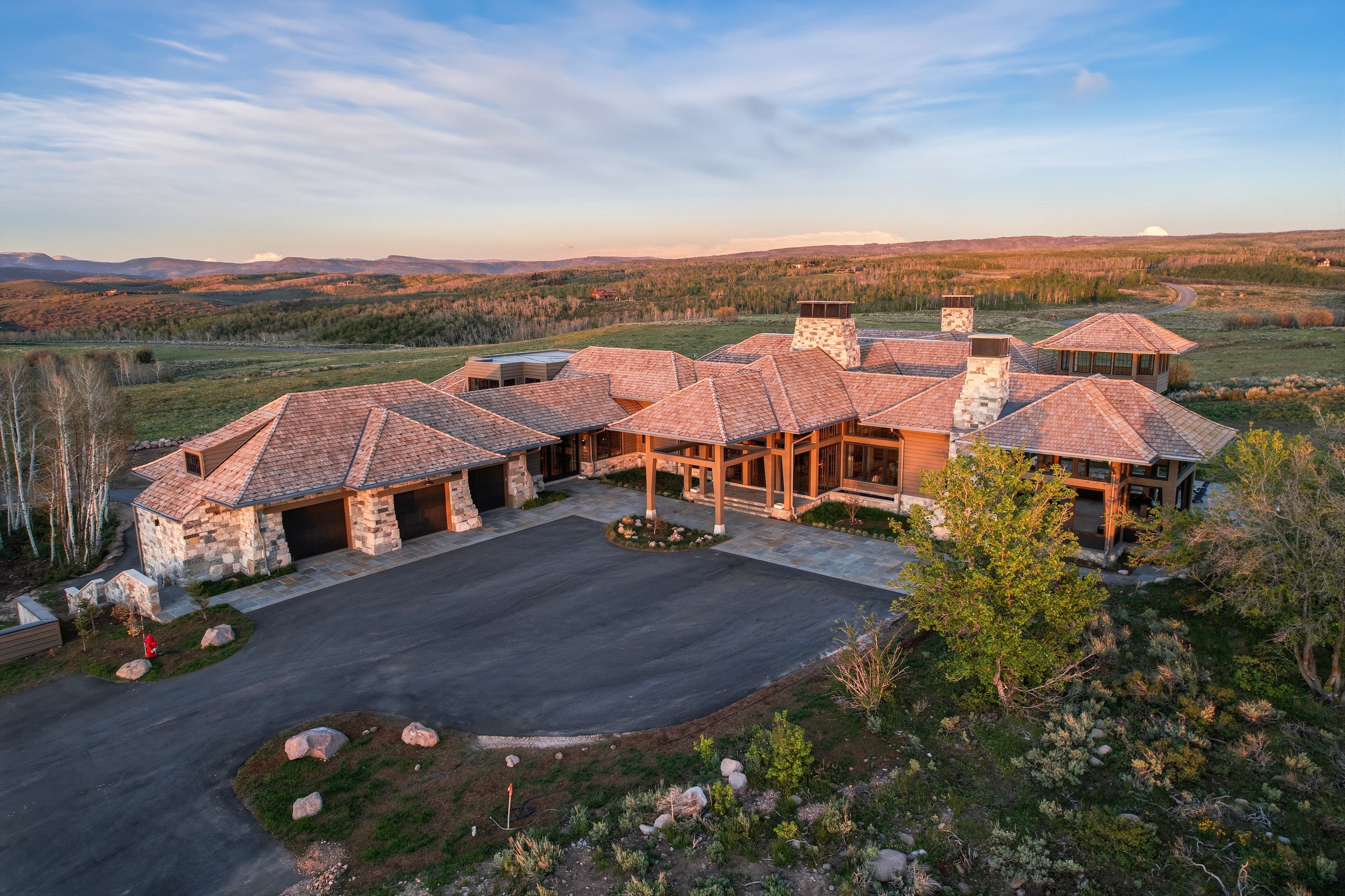 Expansive property featuring a stone and wood beam exterior, multiple attached garages, a large paved driveway, and covered outdoor living areas