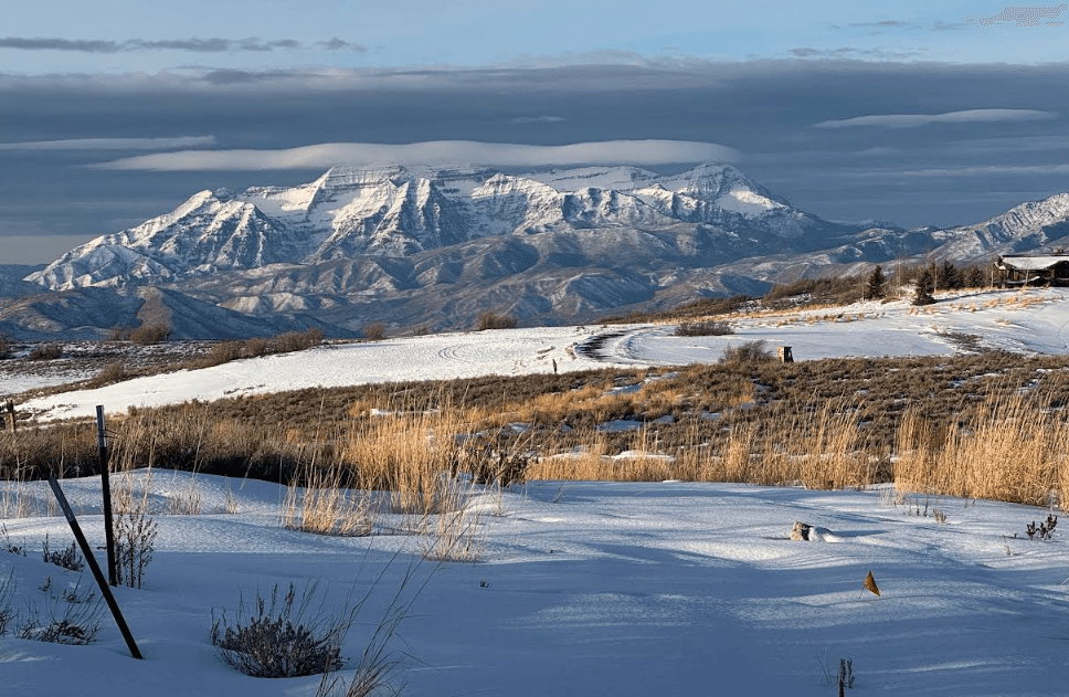 Expansive snow-covered landscape featuring distant snow-capped mountains and a rustic-style structure