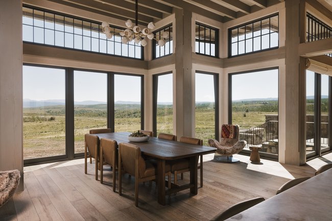 Expansive dining area featuring multiple floor-to-ceiling windows, wood-finish flooring, exposed beam ceiling details, and a contemporary chandelier