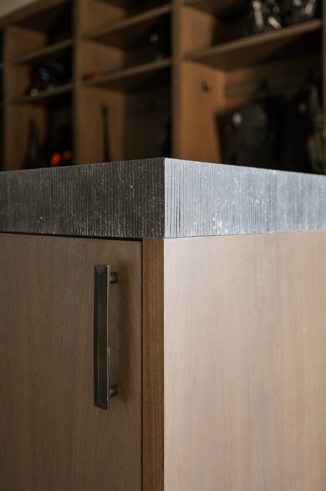 Custom cabinetry featuring a textured stone countertop, light wood-finish door panels, dark wood-finish trim, and a contemporary metal handle