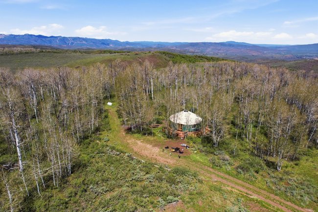 Circular structure with a geodesic dome roof, surrounded by a dense natural tree line