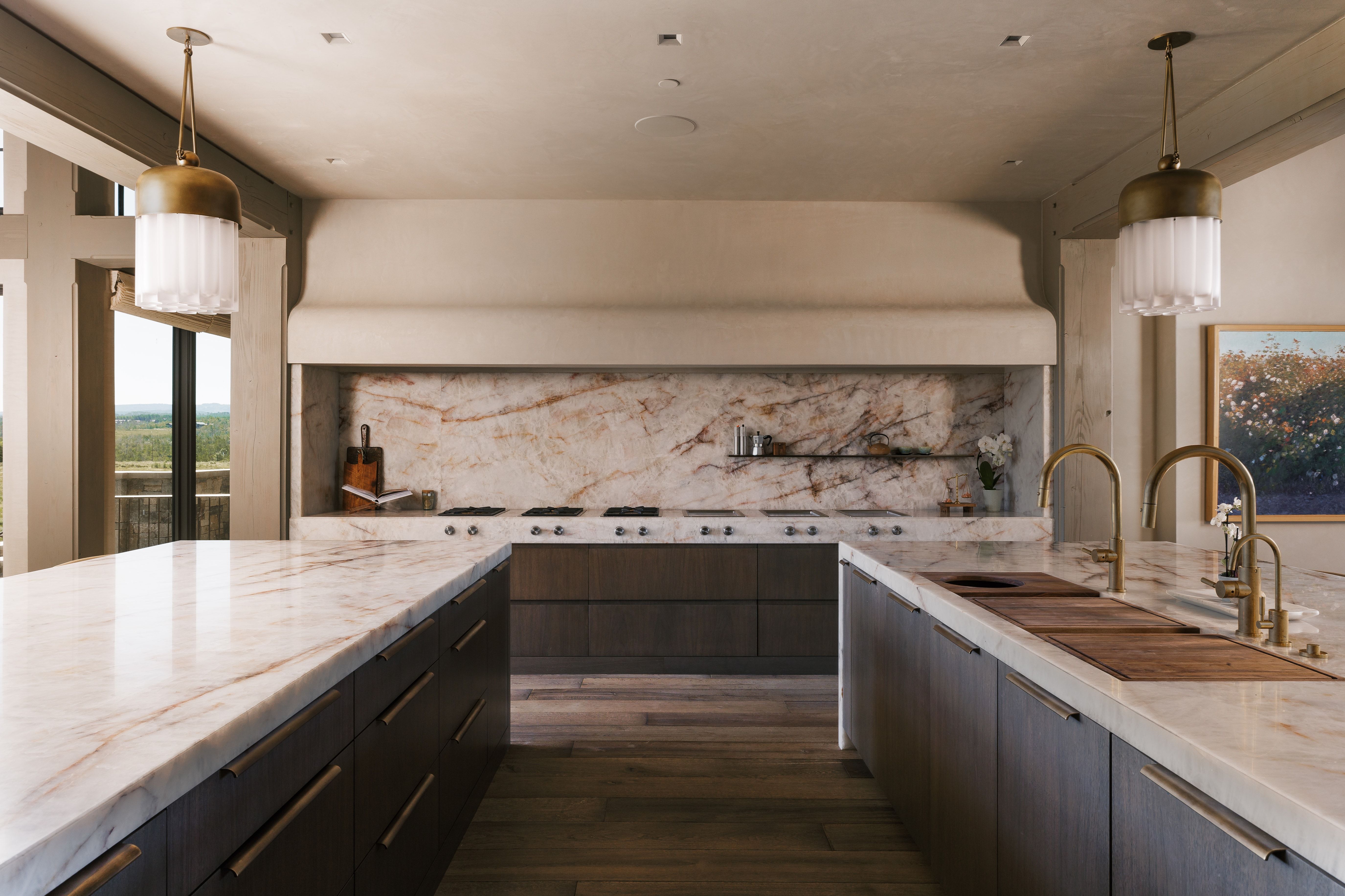 Gourmet kitchen featuring two expansive islands with stone countertops, a professional-grade range, custom dark wood cabinetry, and elegant brass pendant lighting