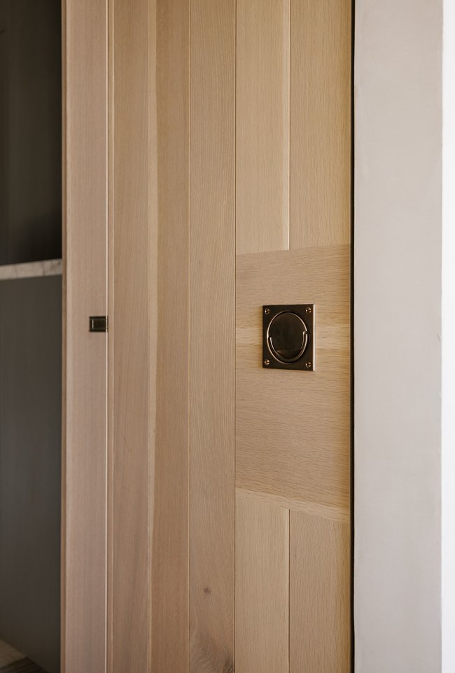Vertical wood paneling with a natural finish, featuring a bronze flush pull handle and a coordinating small bronze latch