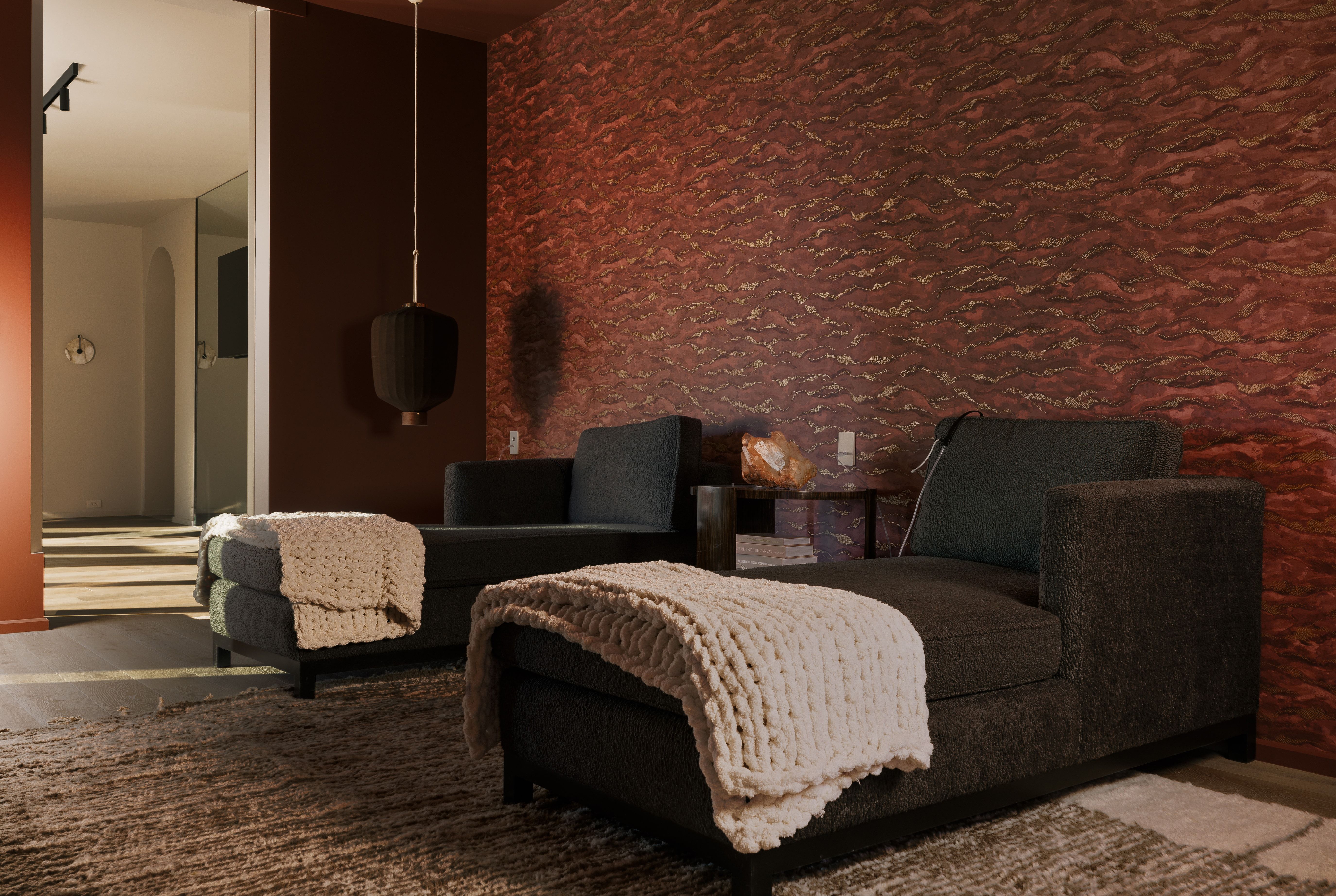 Interior space featuring a textured accent wall with a rich red hue, dark brown wall, and wood-finish flooring