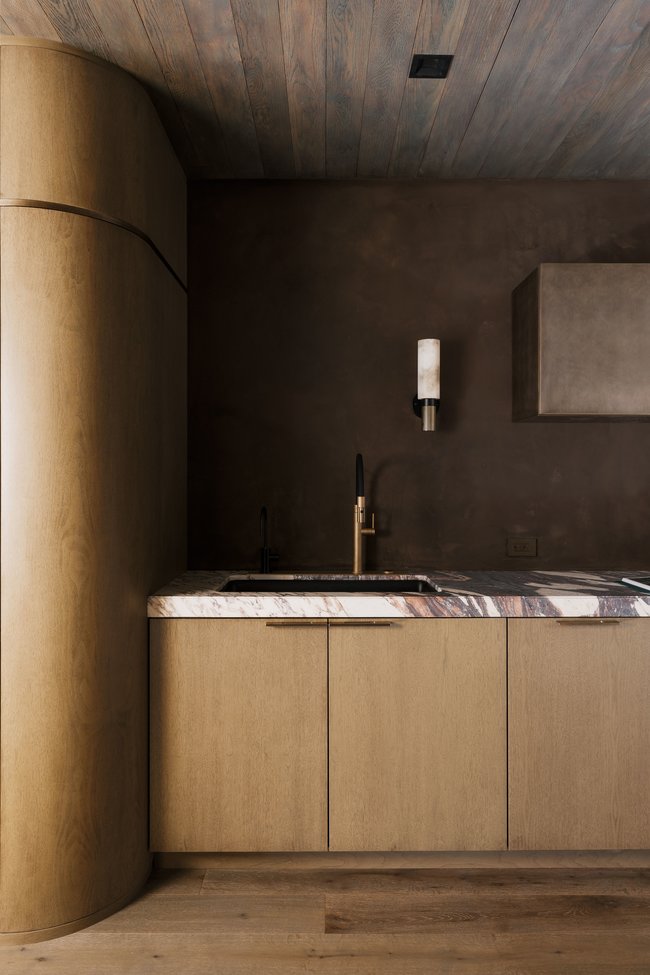 Contemporary wet bar featuring a built-in sink with a gold-tone faucet, wood-finish cabinetry, and a stone countertop