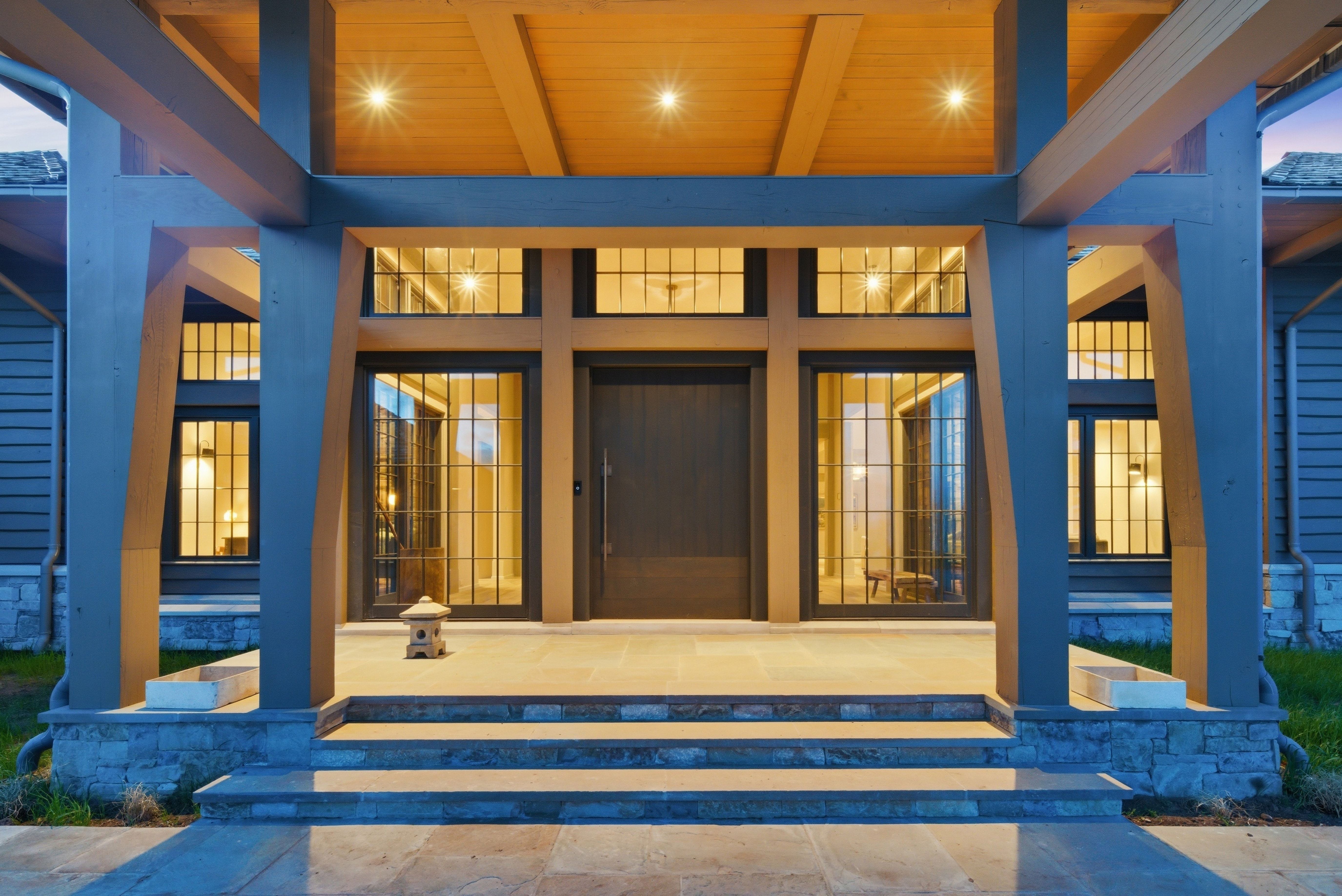 Grand entryway featuring substantial timber columns, a wood-paneled ceiling with recessed lighting, and a dark-toned front door
