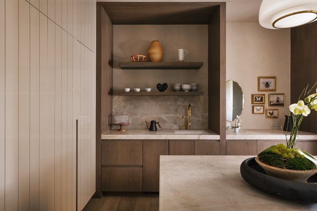 Custom beverage station featuring wood cabinetry, stone countertop, integrated sink with gold-tone faucet, and open shelving