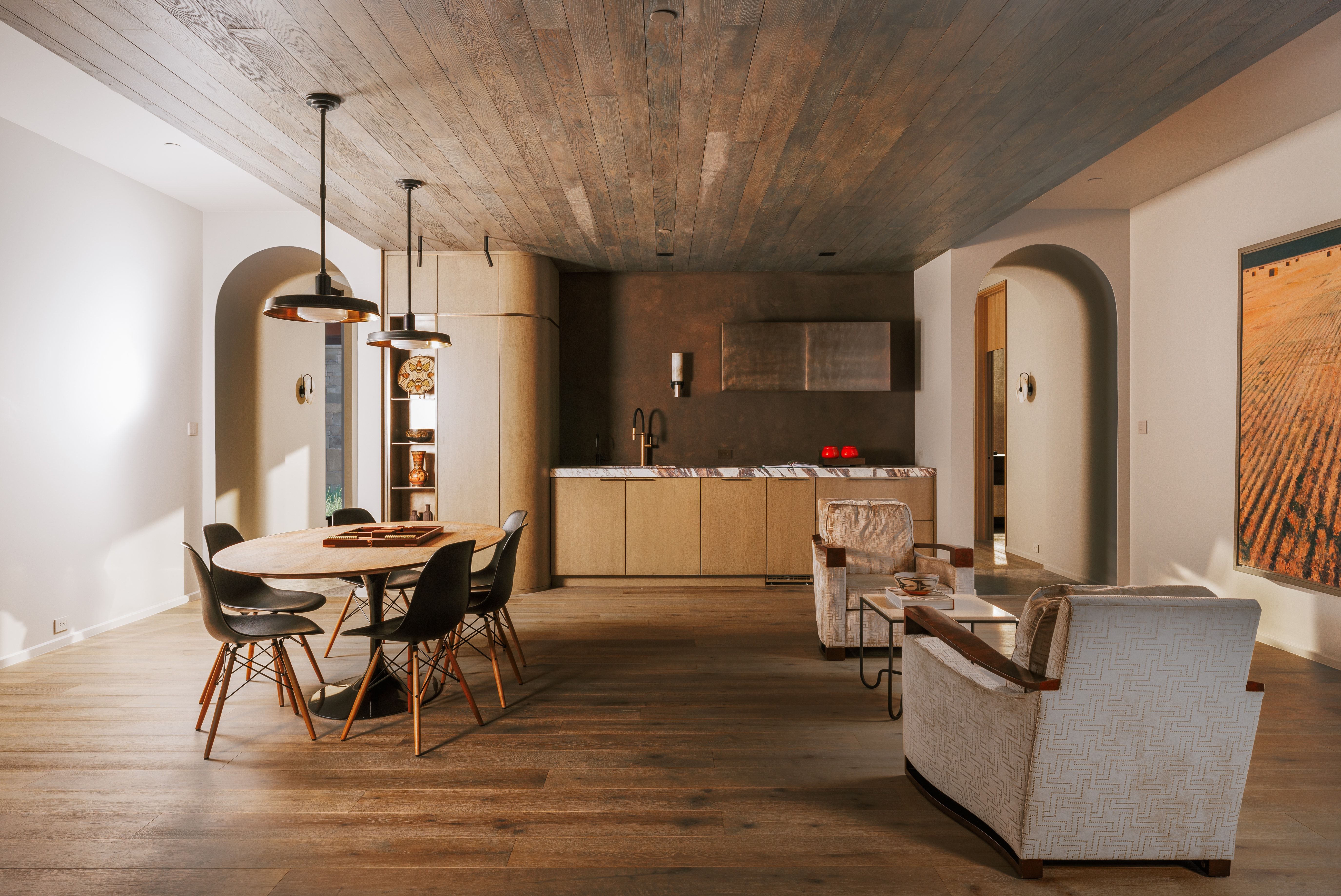 Open-concept interior featuring wood-finish flooring, a wood-paneled ceiling, multiple arched doorways, a built-in wet bar with a stone countertop, and integrated cabinetry