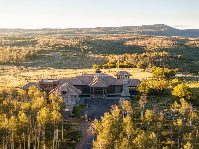 Expansive mountain property featuring a large residence with multiple gabled roofs, stone-clad chimneys, and extensive windowing