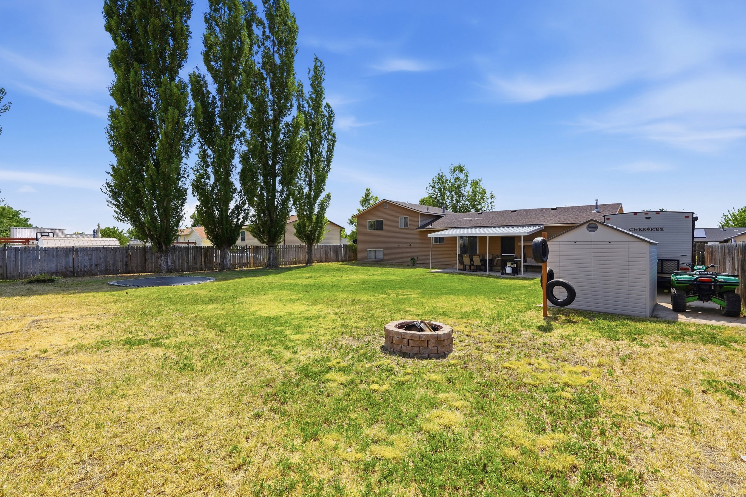 Expansive backyard featuring a stone fire pit, mature trees, a privacy fence, and a covered patio