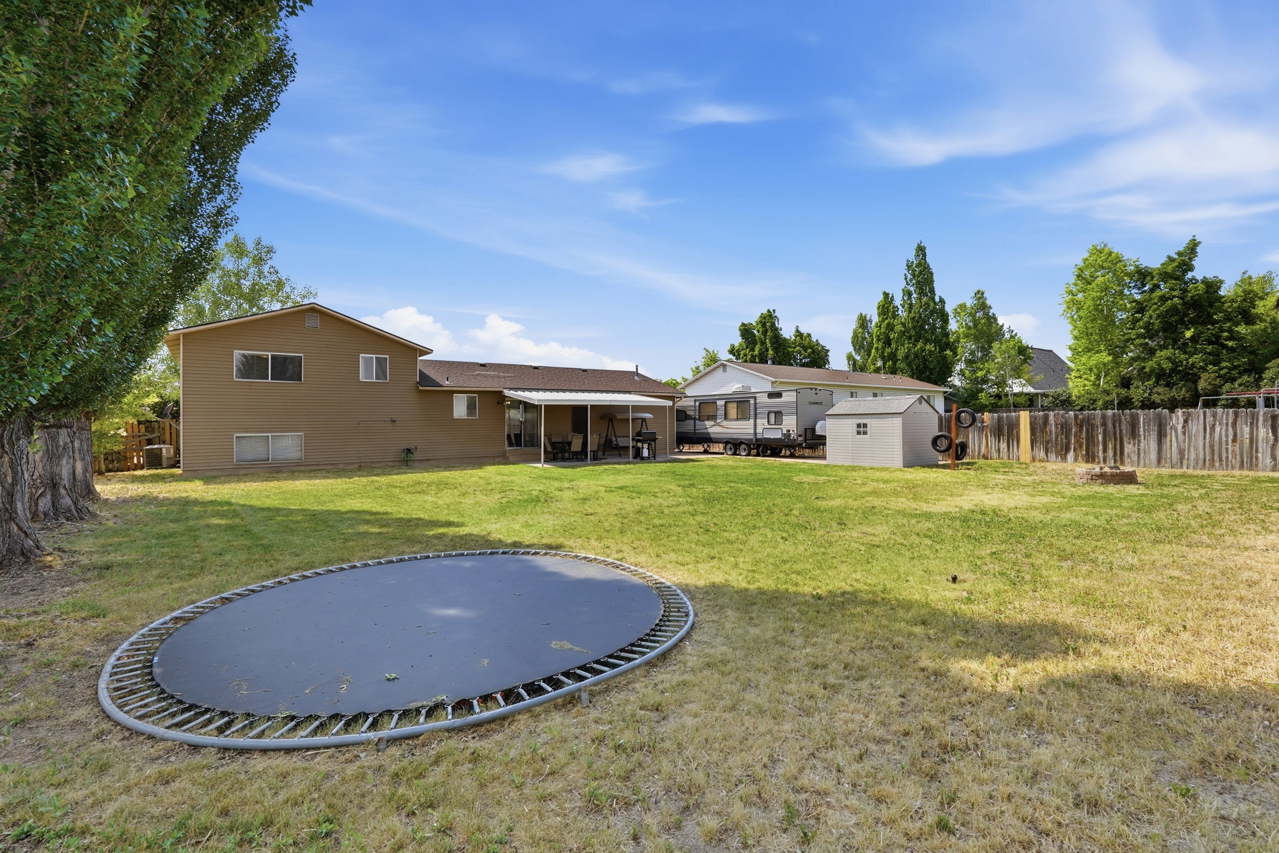 Expansive backyard featuring a manicured lawn, a covered patio, and a storage shed