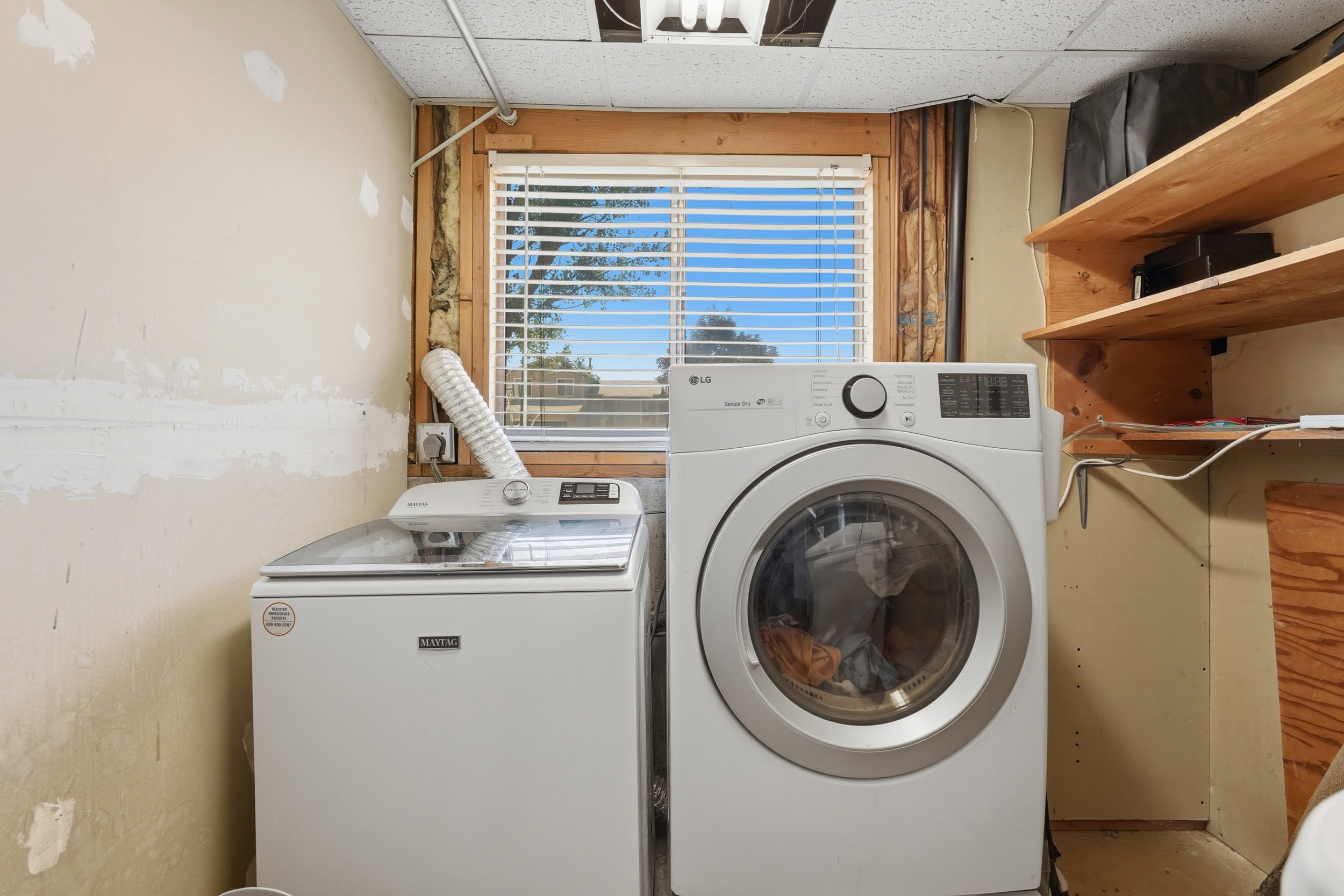 Laundry area featuring a window with blinds, wood-frame window, and wood shelving