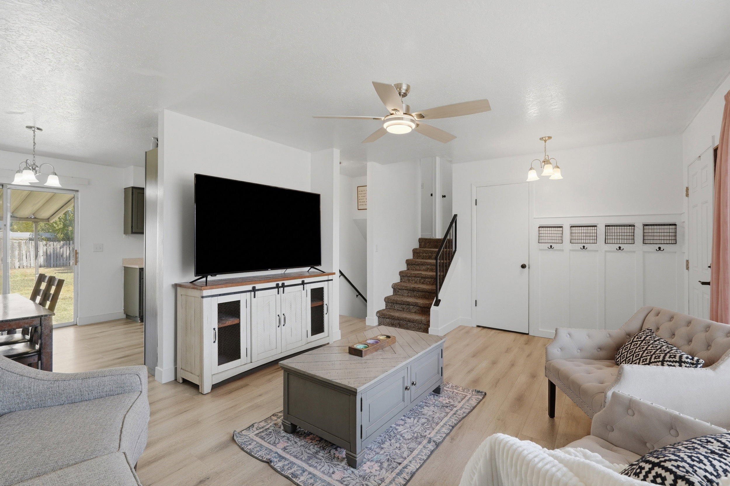 Spacious living area featuring light wood-finish flooring, a contemporary ceiling fan with integrated lighting, and a neutral color palette