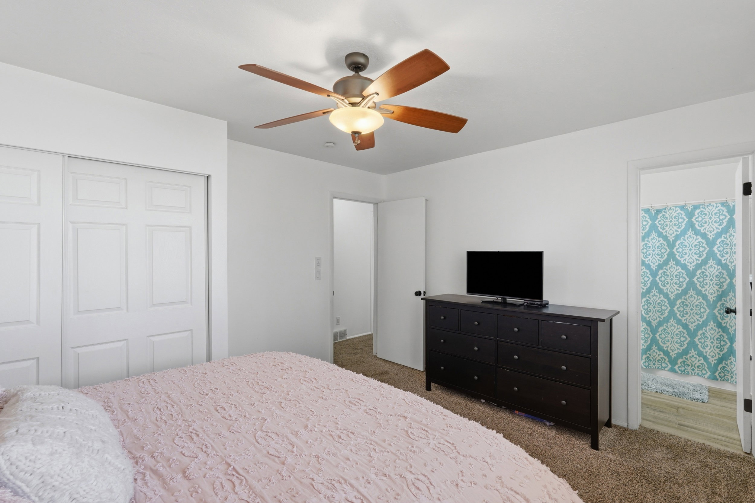 Carpeted room featuring a ceiling fan with integrated lighting, white walls, and bi-fold closet doors